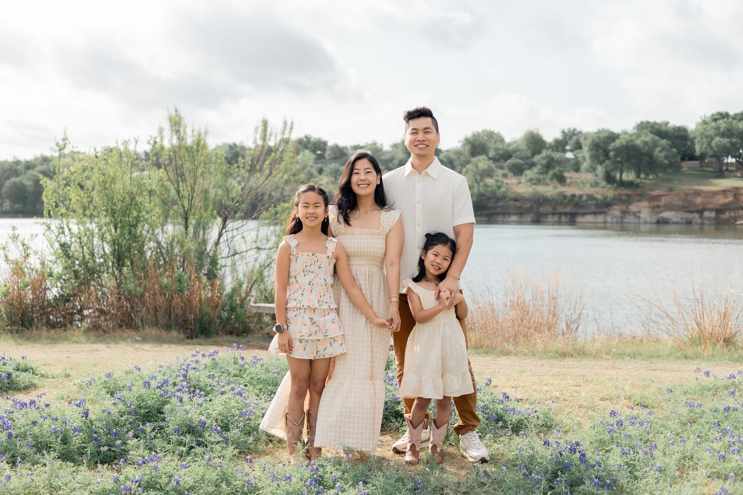 Family holding hands hugging one another during a family lifestyle session in a field of blue bonnets near a lake