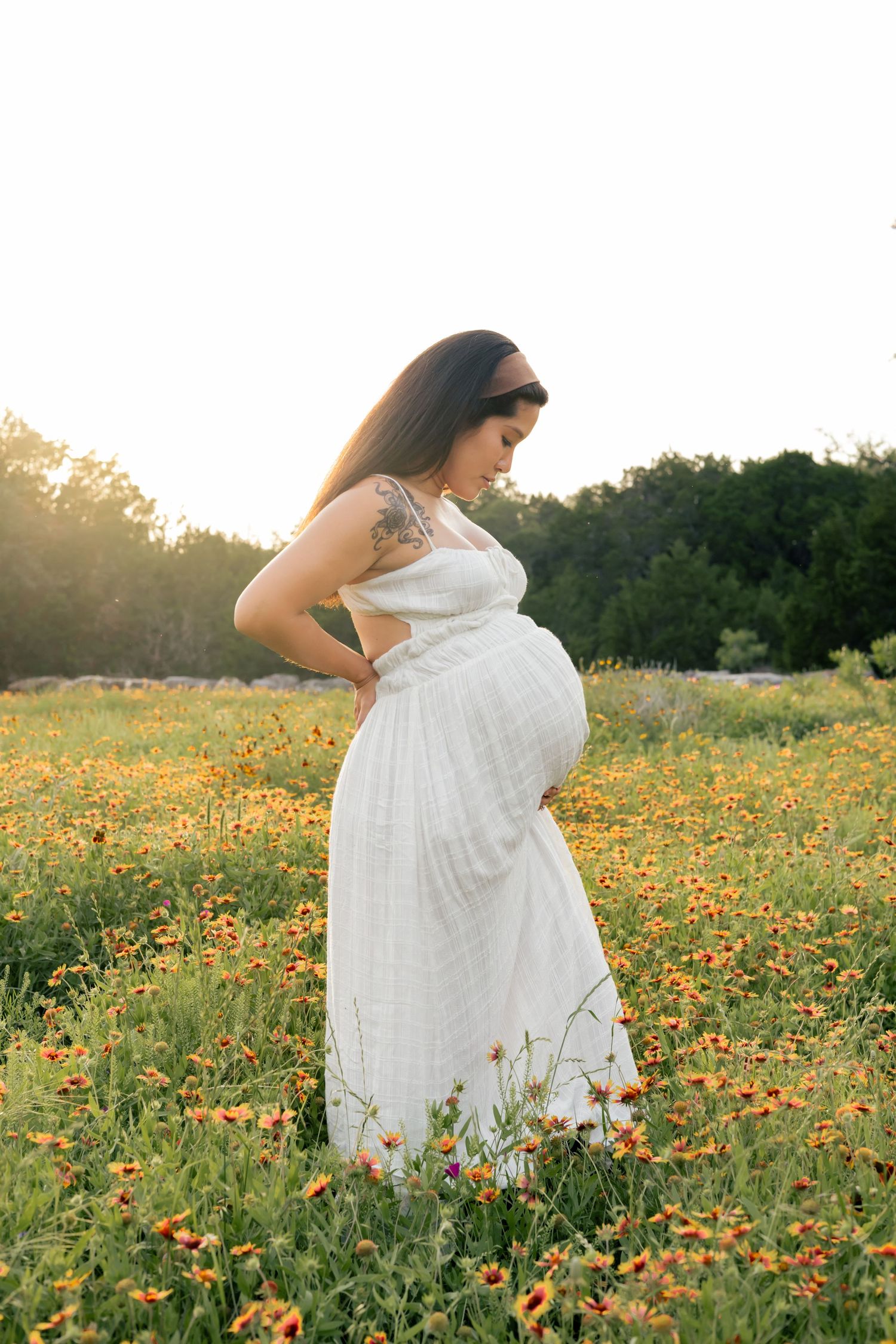 Pregnant mother to be looking at her belly in a grassy field of wildflowers during a sunset maternity session