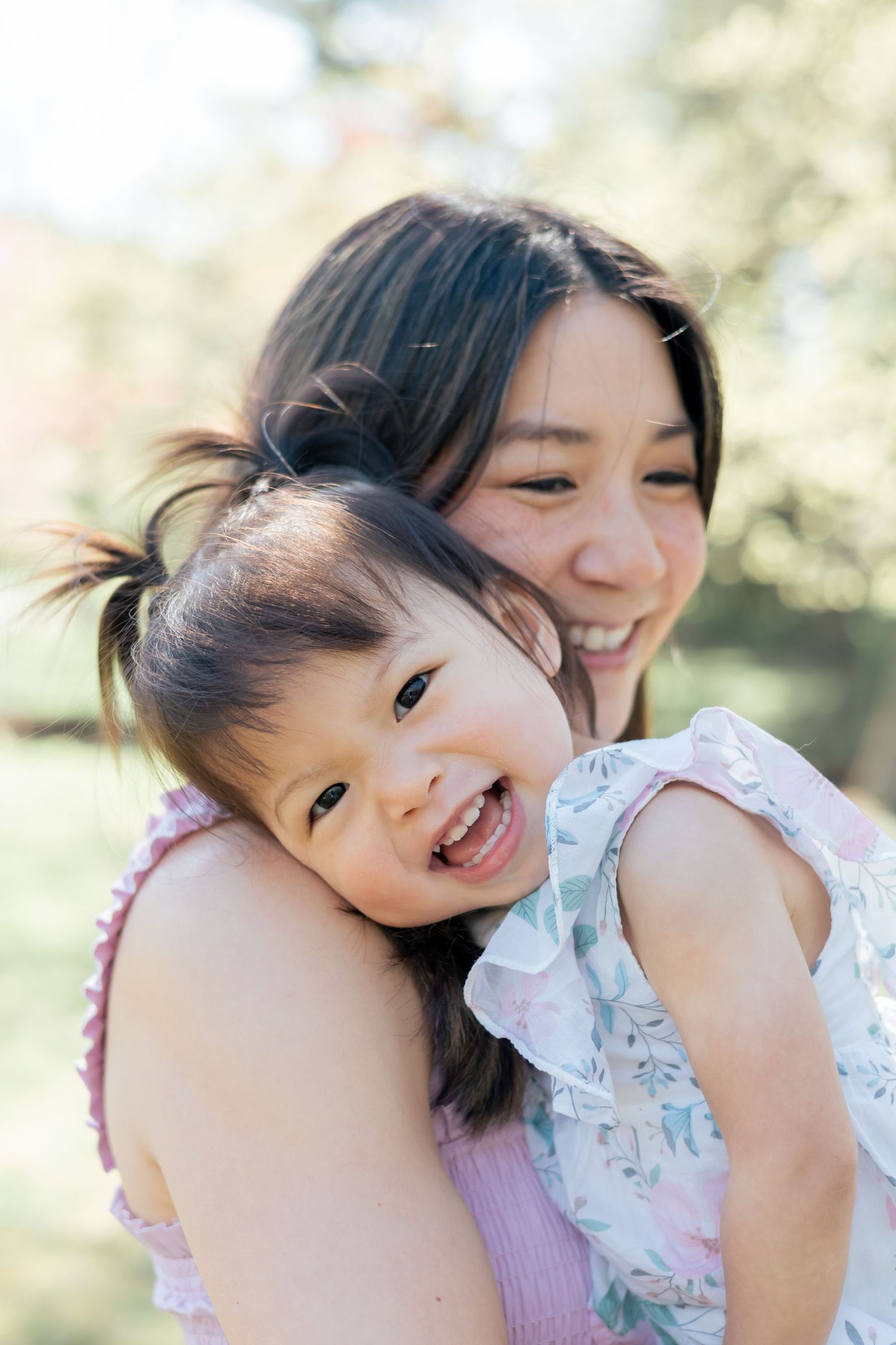 Young toddler laughing at the camera hugging her mom during a lifestyle family session outdoors in the park