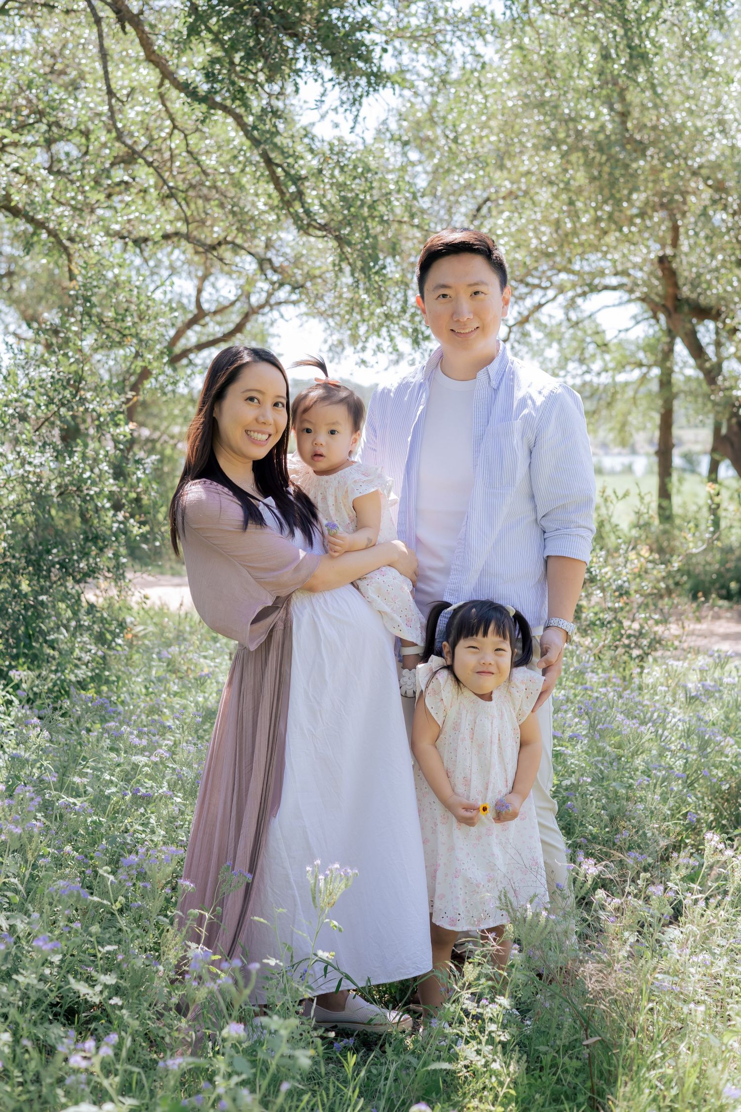 Family smiling together at the camera in a park filled with lush green trees during a lifestyle family maternity session