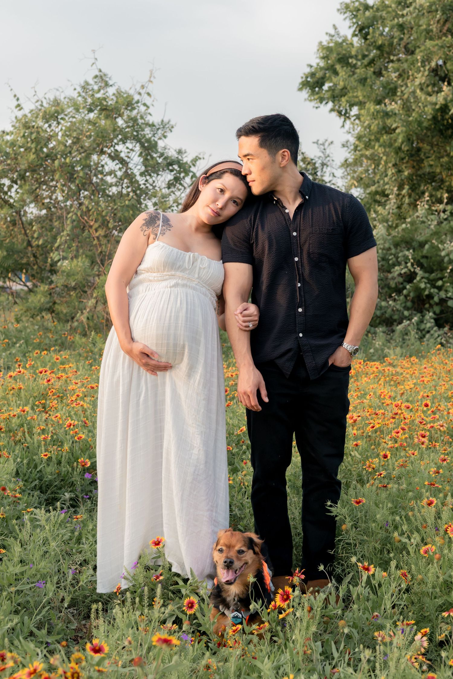 Pregnant Couple expecting their first child embracing each other in a grassy field of wildflowers together during a sunset maternity session