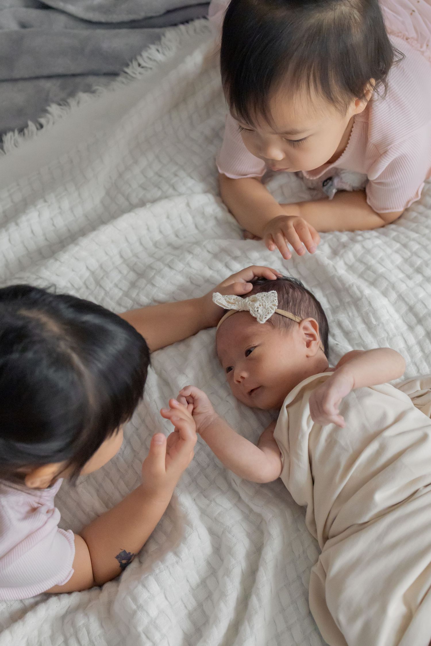 Siblings playing with newborn baby at home during a natural light lifestyle newborn session