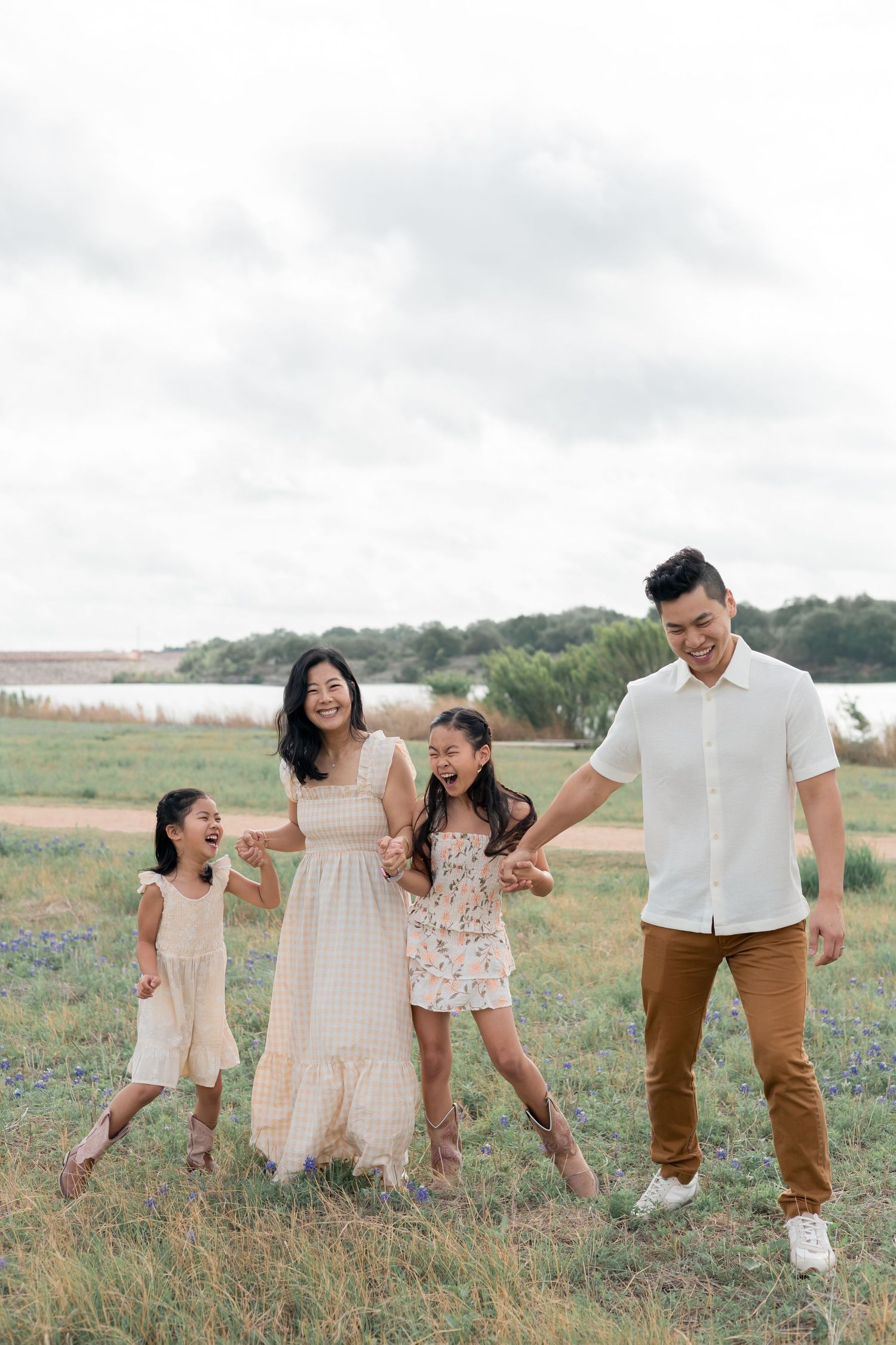 Family holding hands, laughing and walking together during a natural light lifestyle family session in a field of blue bonnet flowers