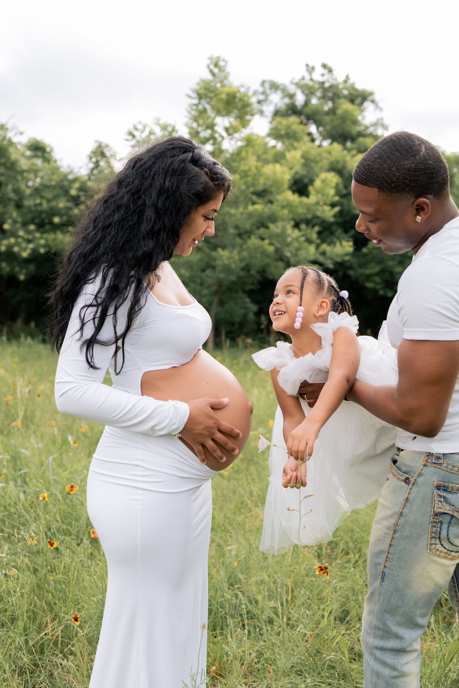 Family smiling at one another embracing mom's belly bump as they wait for their newborn baby to arrive