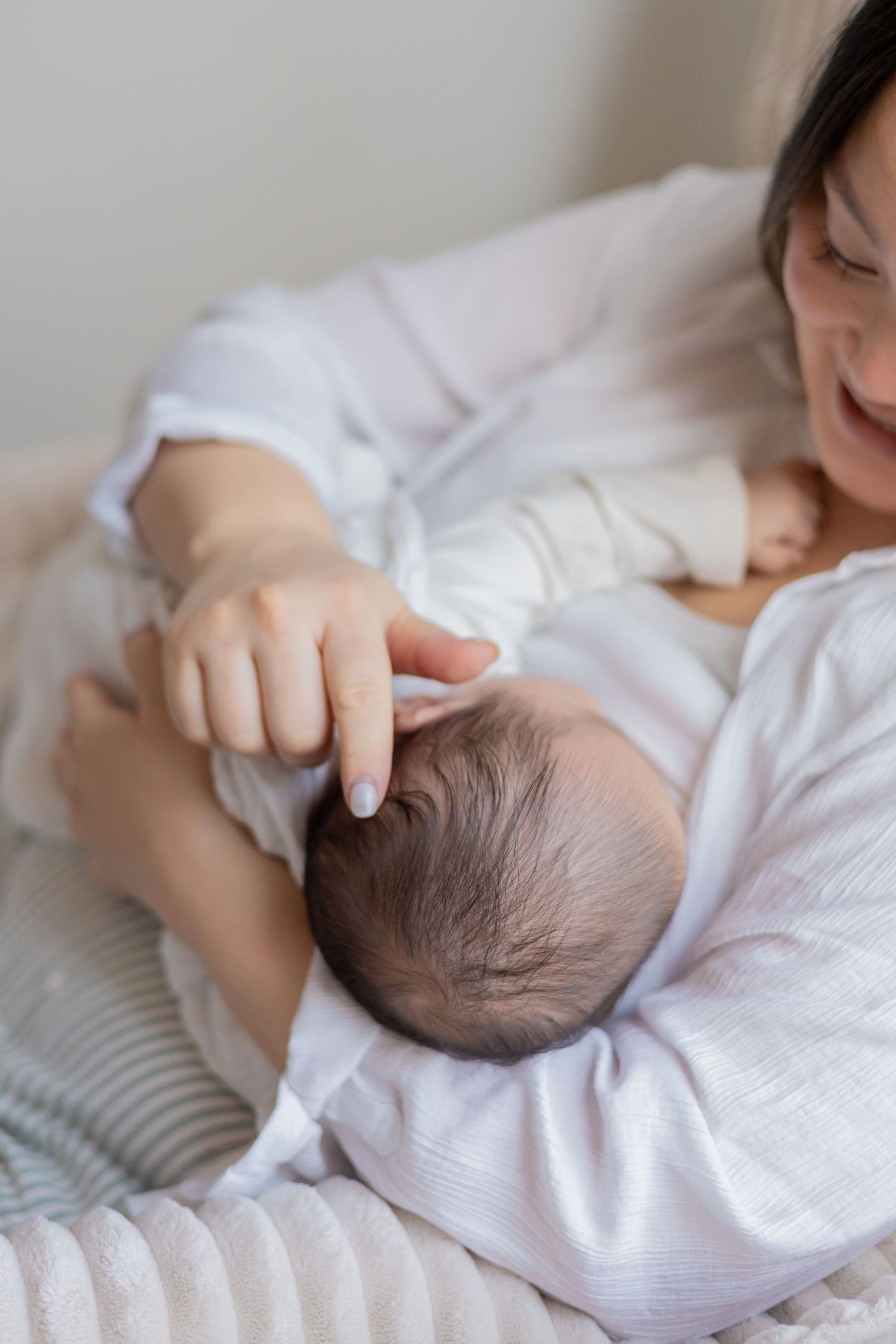 Mother stroking her baby's head while he is breastfeeding during a natural light in home newborn session