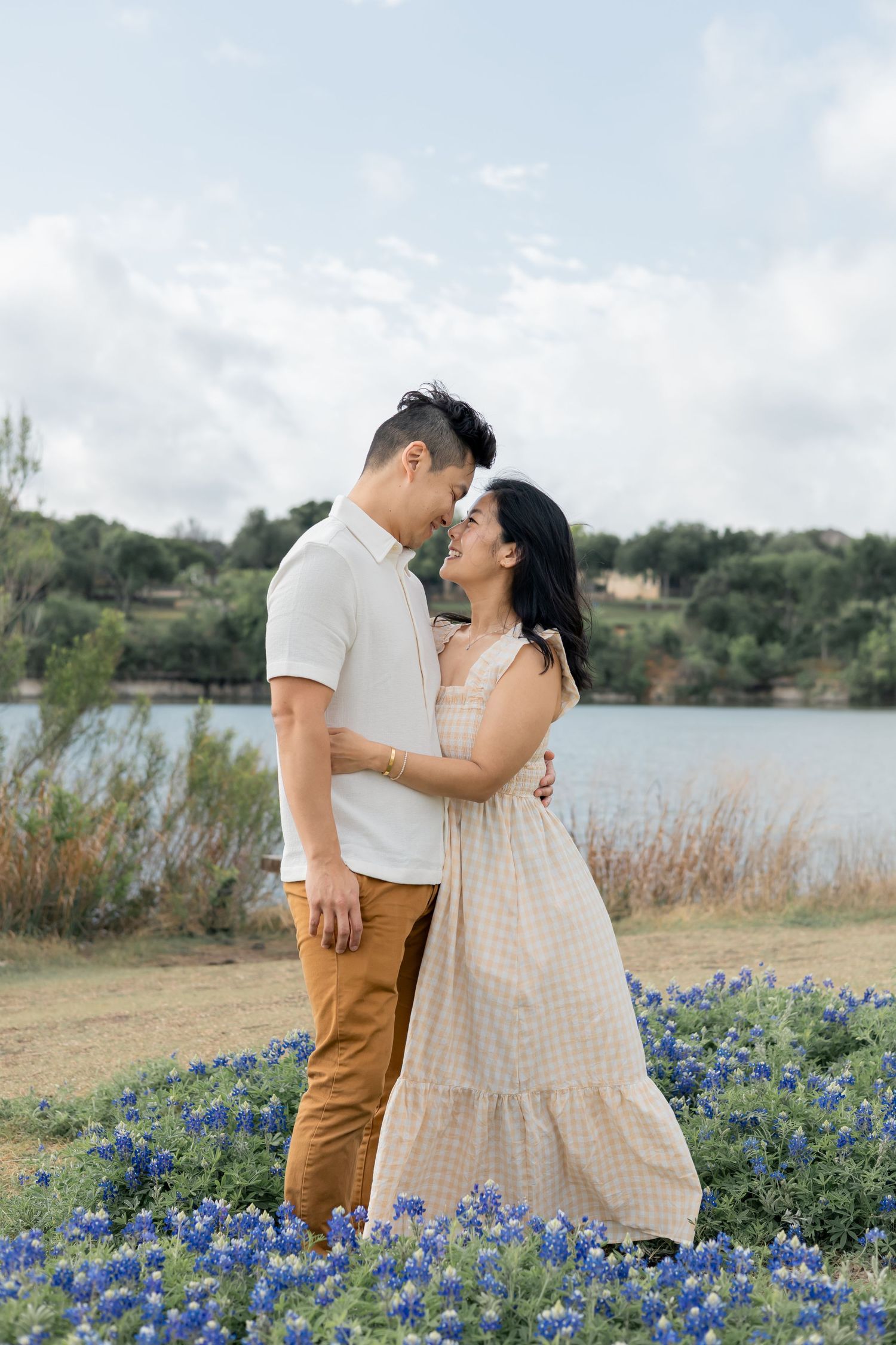 Couple gazing up at one another nose to nose during a family lifestyle session outdoors in a field of blue bonnets by a lake