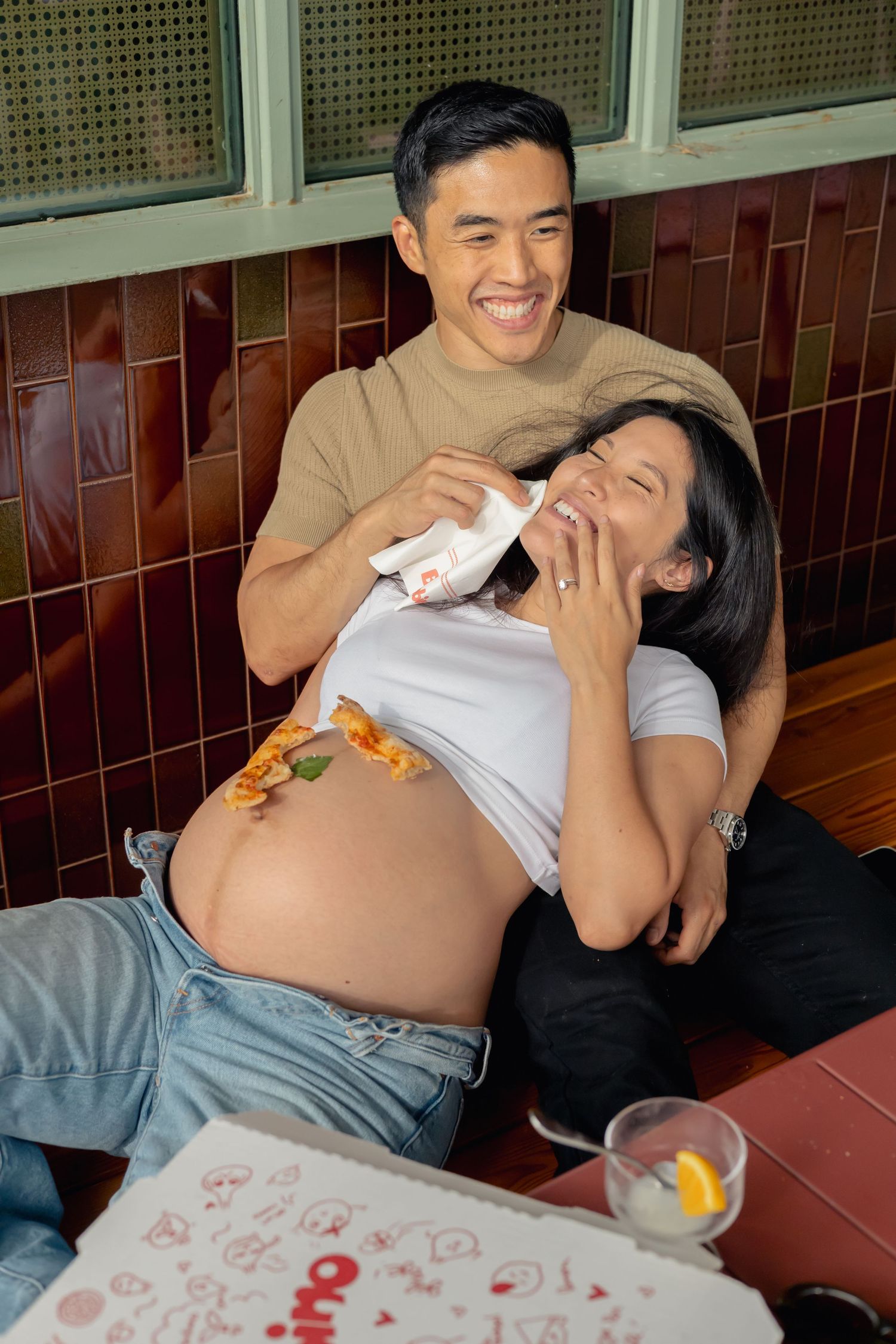 Couple laughing and being silly together while eating pizza during their pizza date maternity session