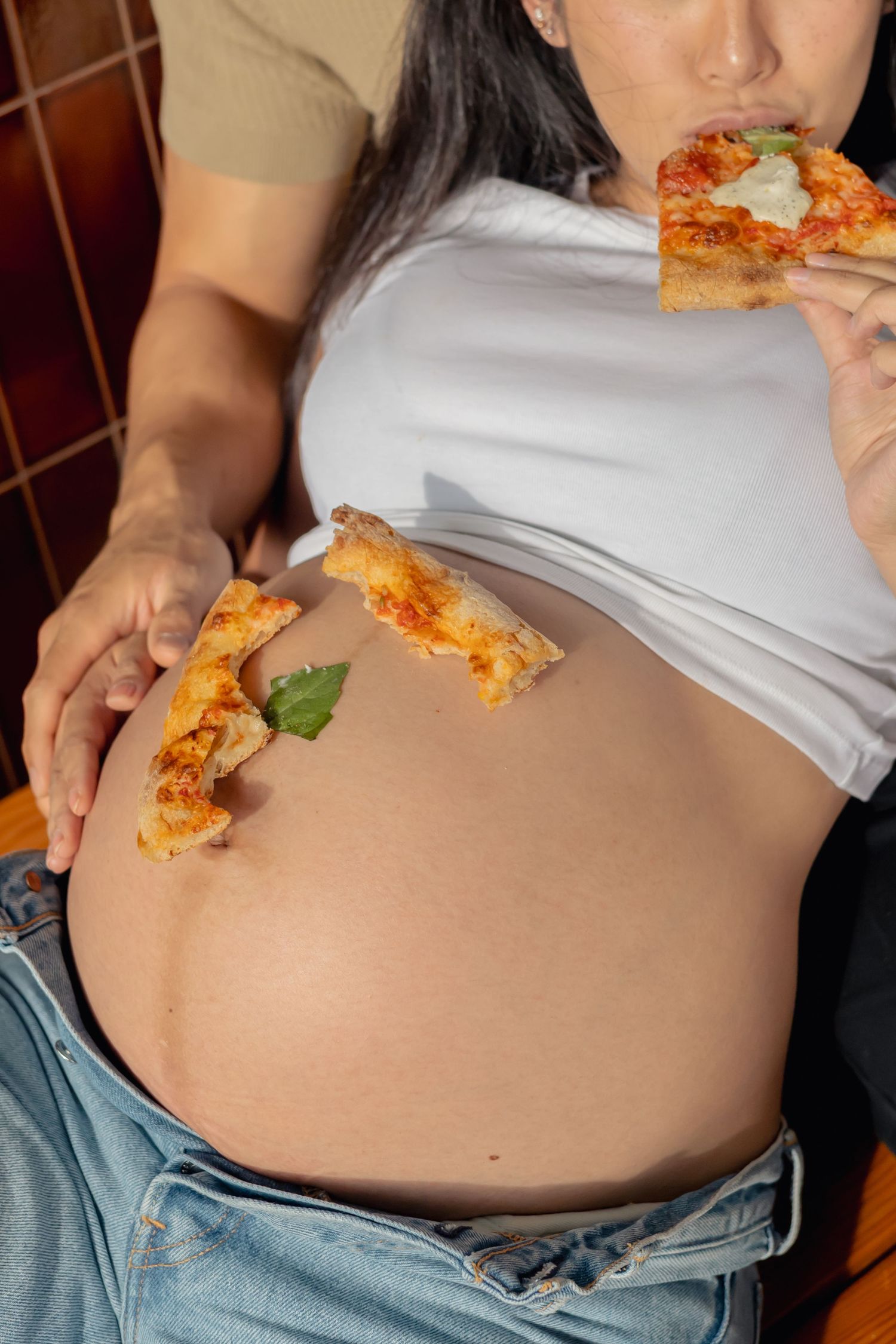Closeup of hands on a pregnant belly with pizza crust during a lifestyle maternity pizza date session