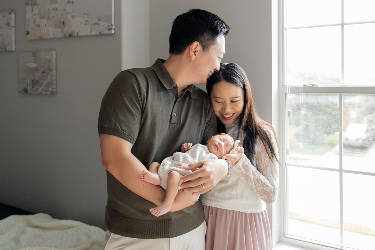 Husband kissing his wife's head as she gazes on her newborn baby during an in home lifestyle newborn session