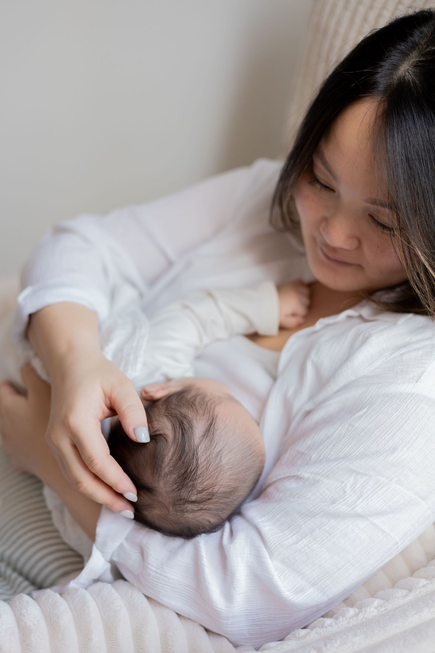 Mom stroking her newborn baby head while she is breastfeeding him during an in home newborn session