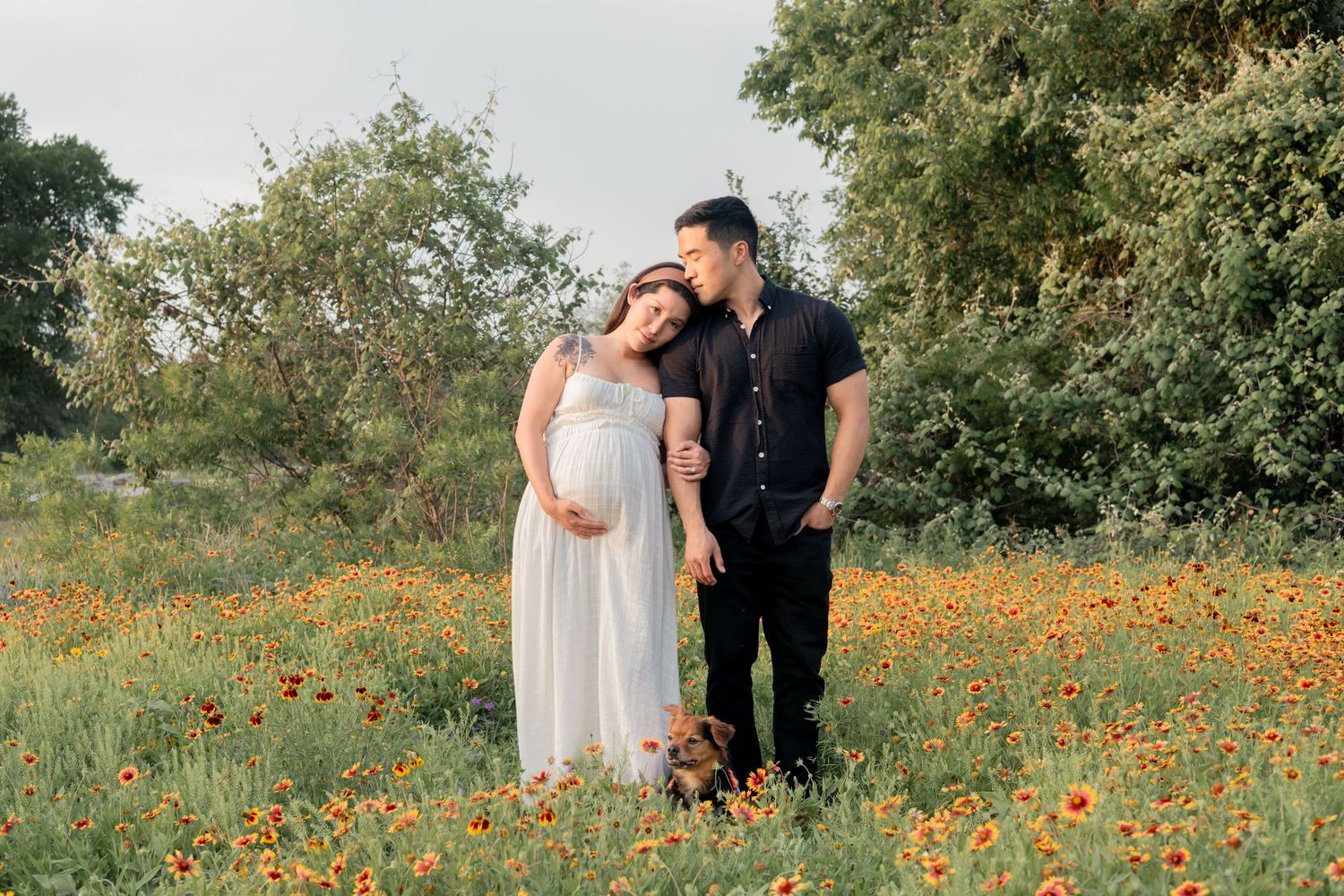 Couple leaning on each other during a lifestyle maternity session in a park with wildflowers