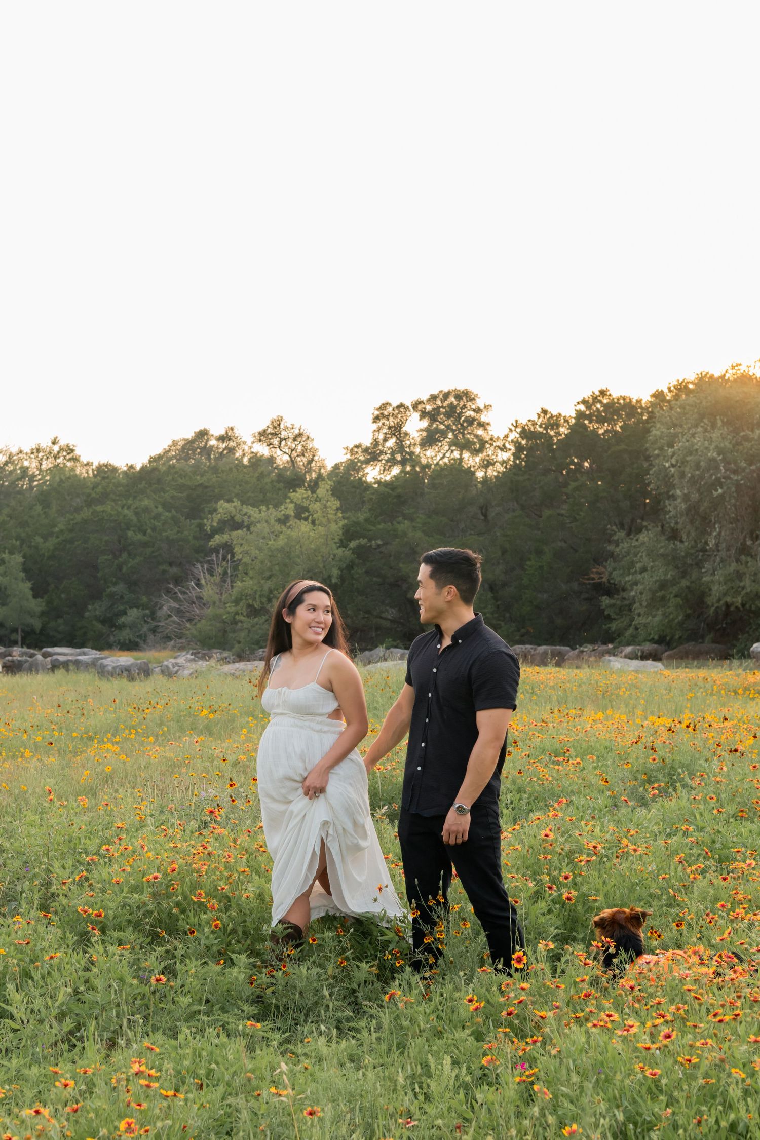 Pregnant Couple expecting their first child walking in a grassy field of wildflowers together during a sunset maternity session