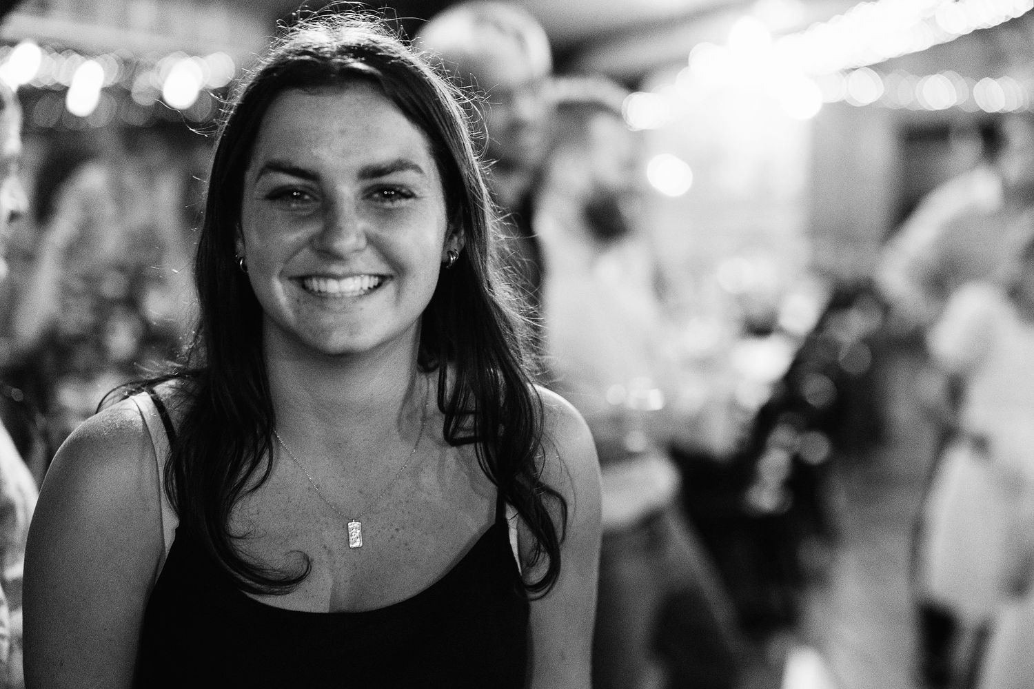 Black and white portrait of a smiling young woman with dark hair at a lively social gathering.