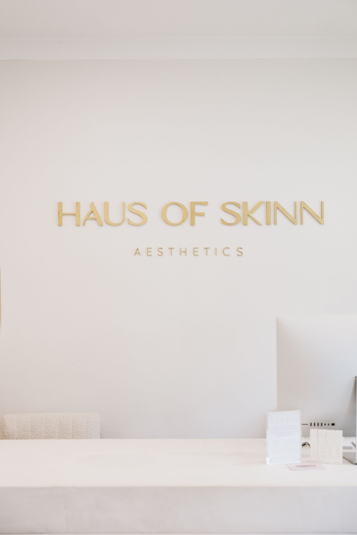 Gold lettering Haus of Skinn Aesthetics logo on white wall above a clean modern reception desk.