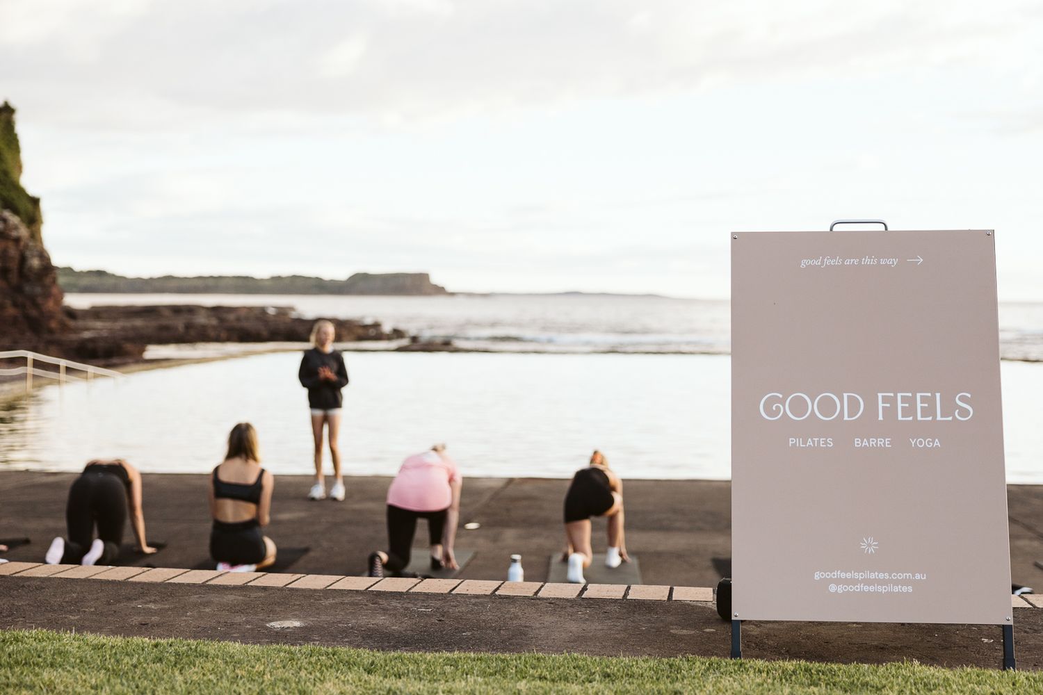 Good Feels outdoor fitness class sign near oceanside workout session at coastal location.