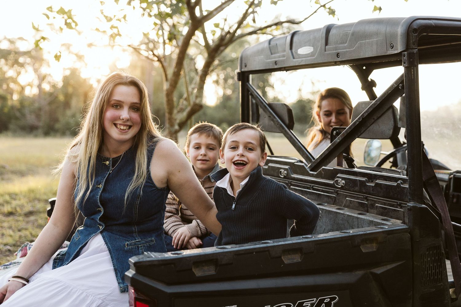 Family of four smiling together on a Ranger UTV outdoors at golden hour.
