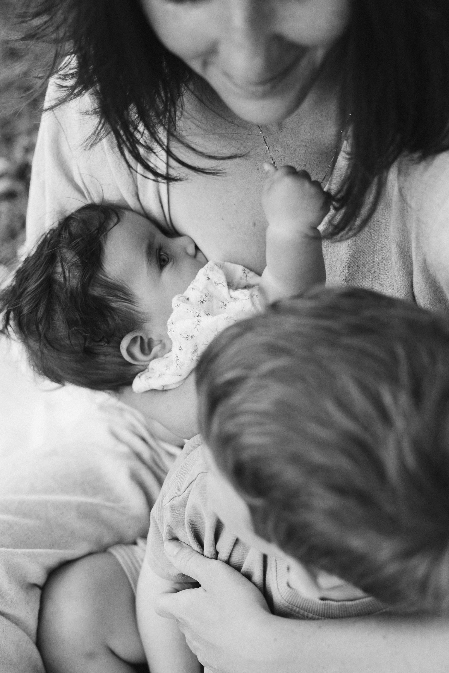 Black and white photo of mother cradling newborn while older child looks on tenderly.