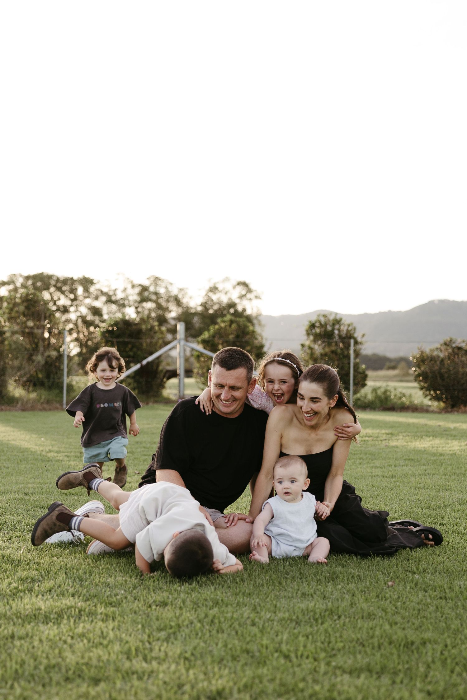 Happy family of five relaxing on green grass at sunset in outdoor setting.