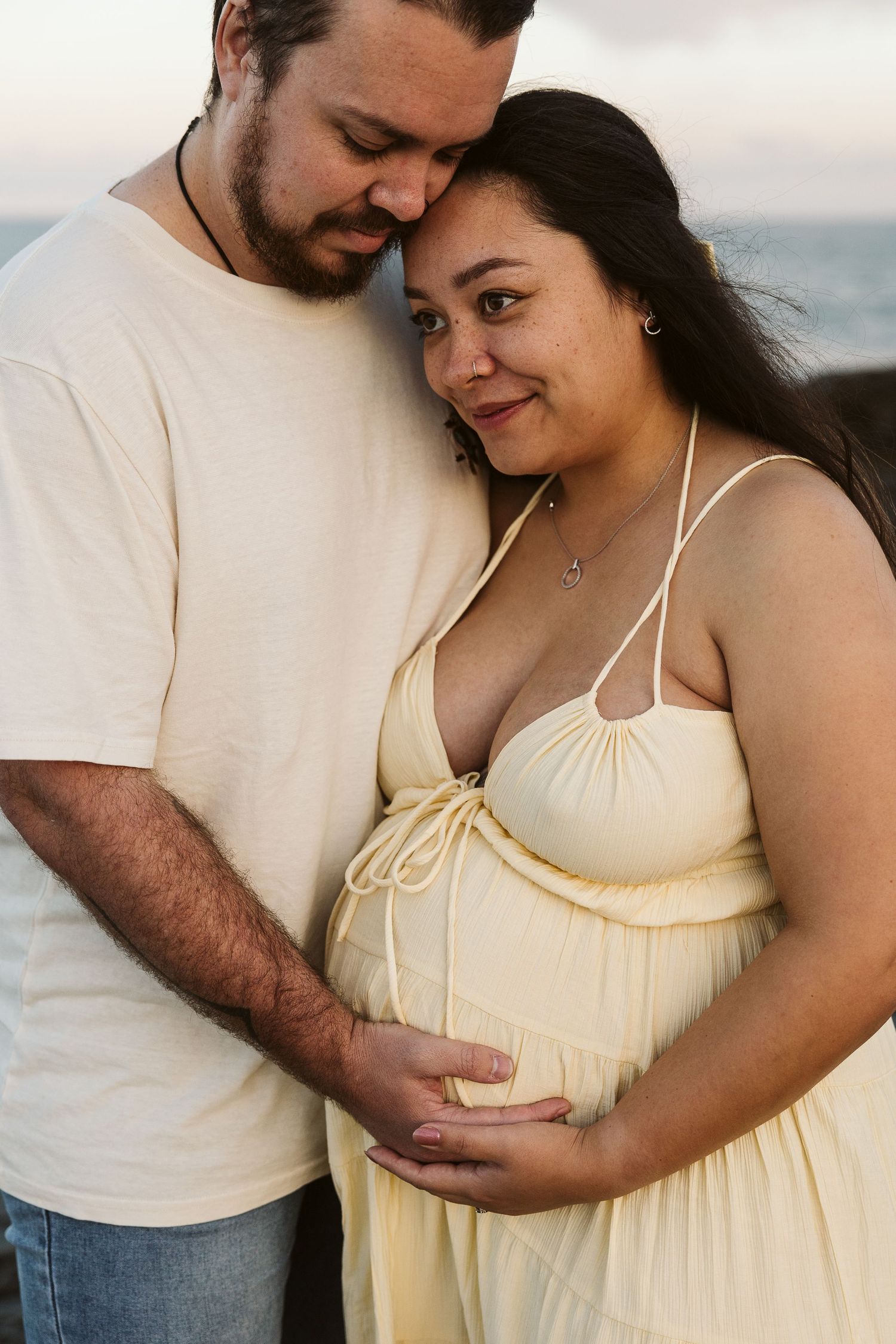 Couple tenderly embracing at sunset, pregnant woman in yellow dress with partner.