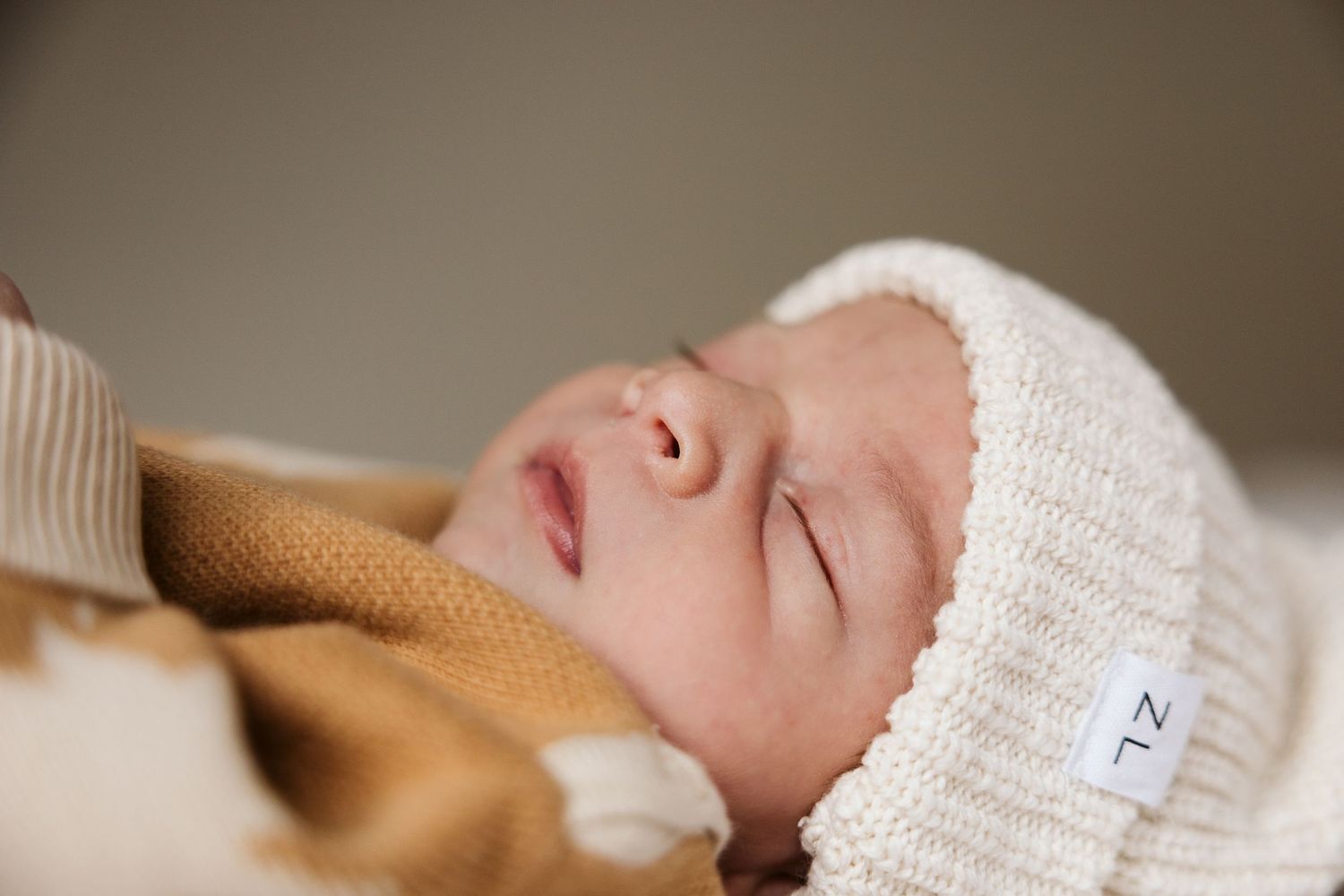 Peaceful sleeping newborn baby wearing cream knit hat bundled in warm blankets.