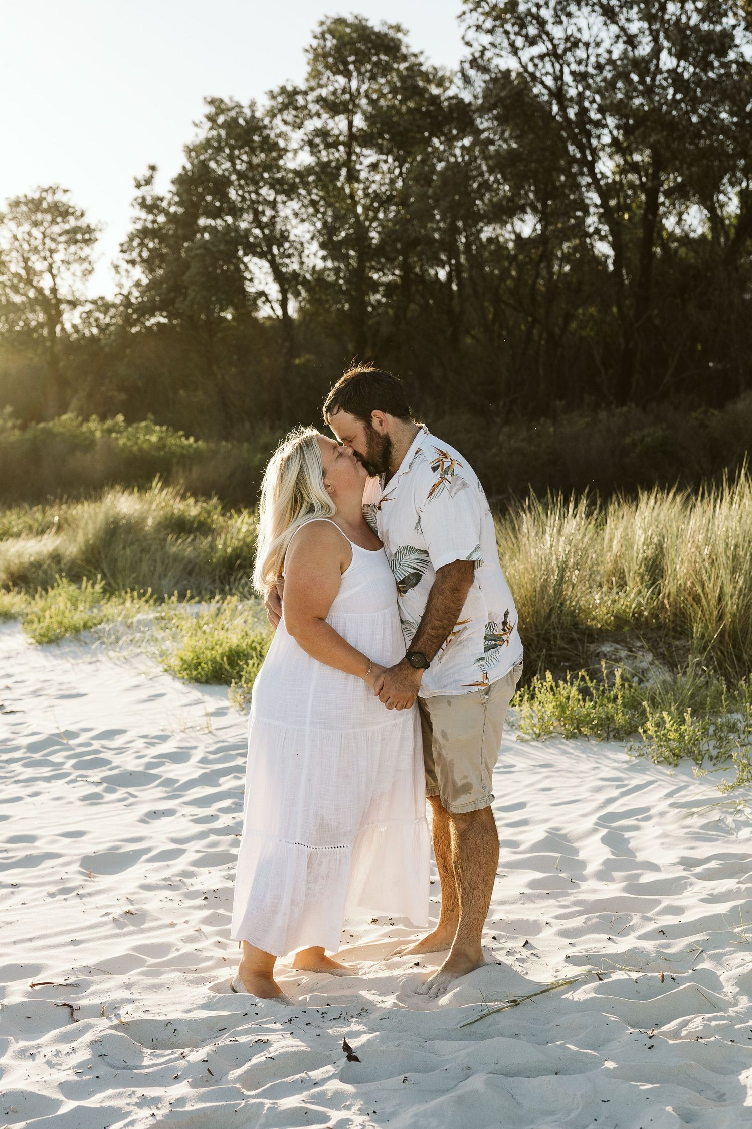 Couple sharing a kiss on white sand beach during golden hour.