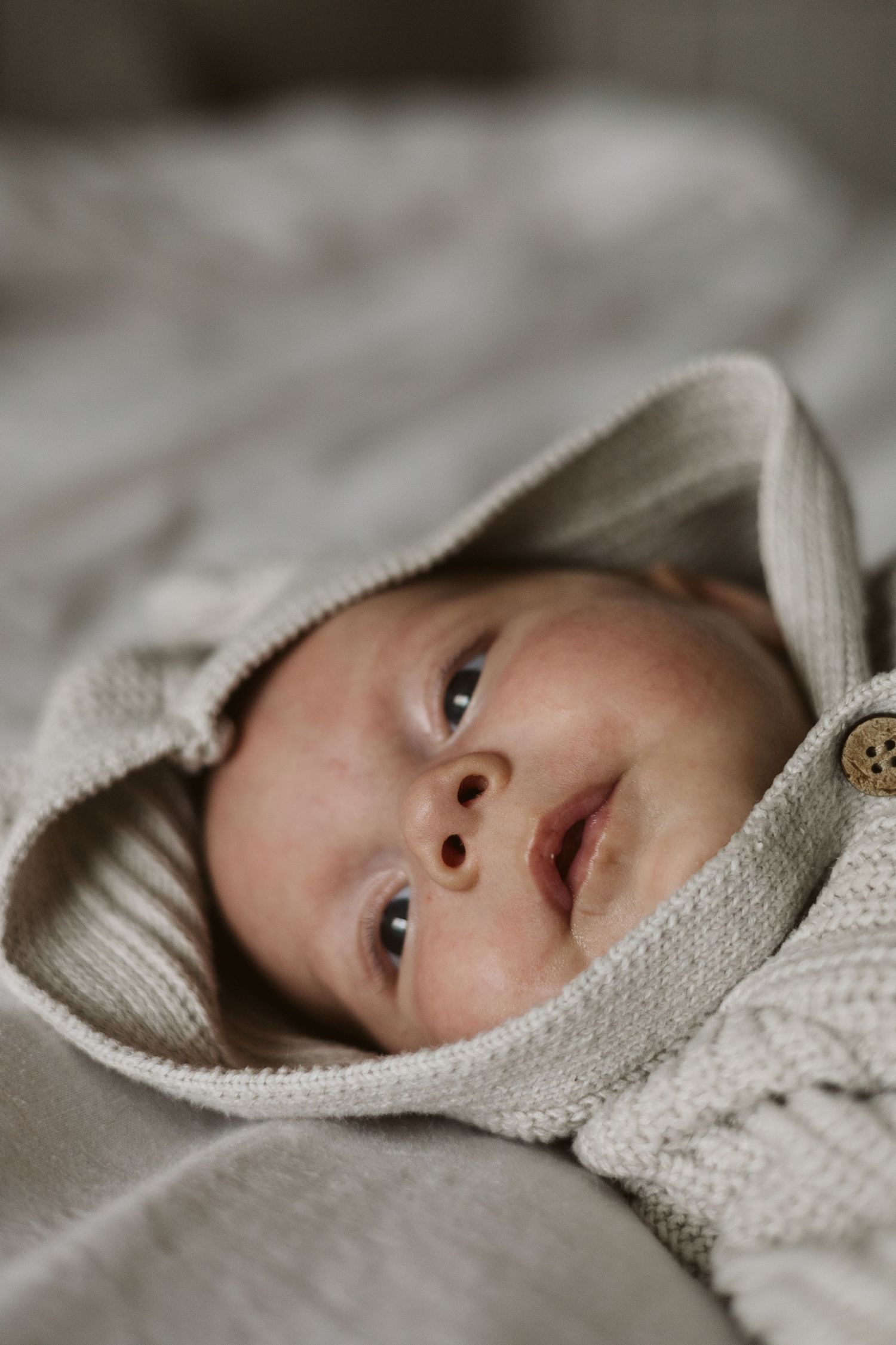 Close-up of peaceful newborn baby wrapped in a cozy hooded knit outfit.