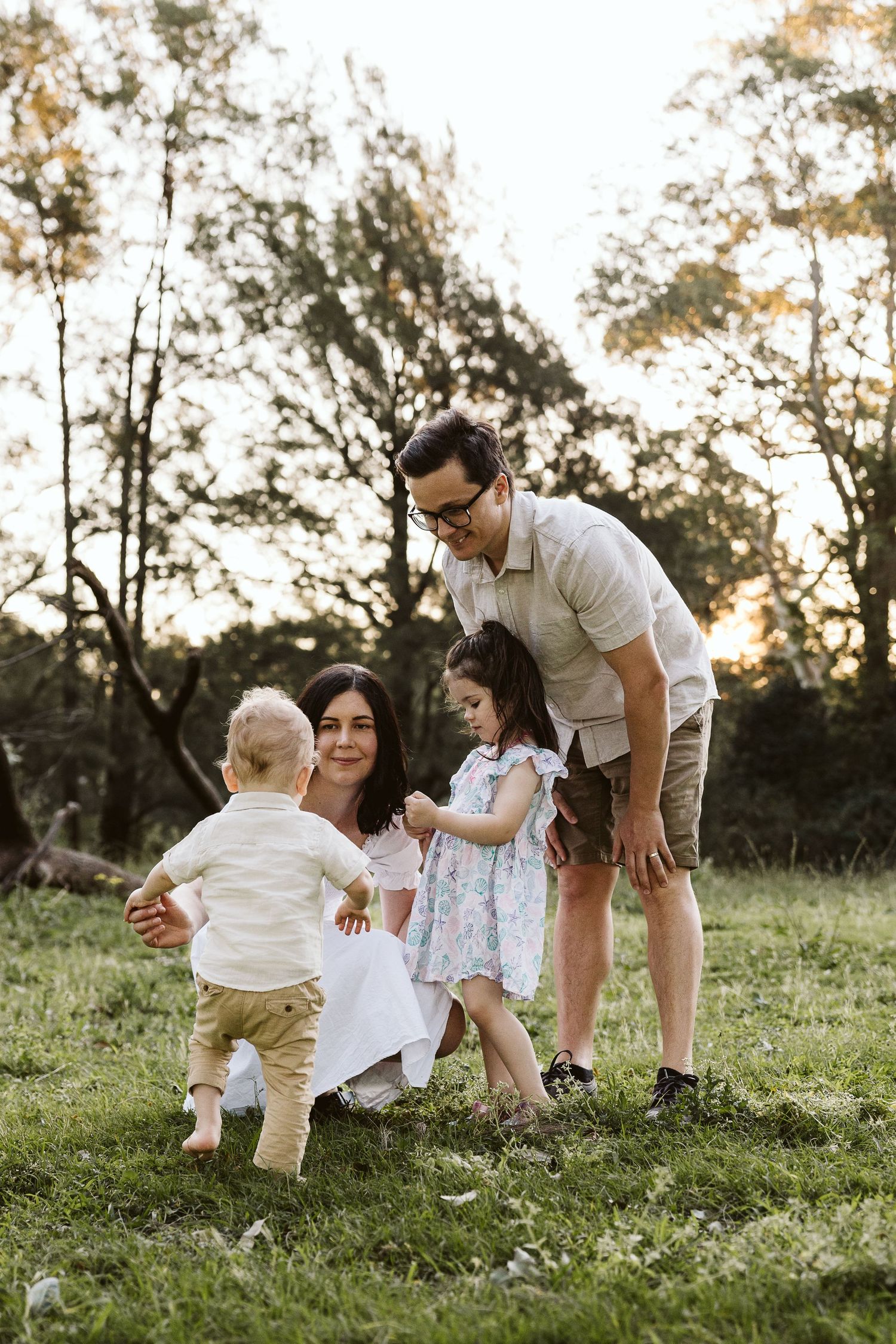 A happy family with two young children enjoys a golden hour outdoor session on a green grassy field.