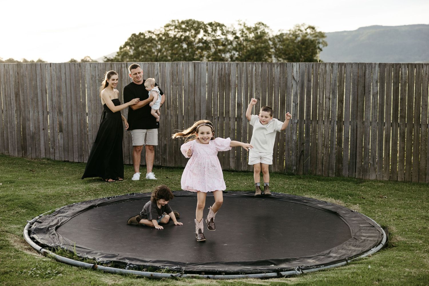 Lively family with children playing and jumping on an in-ground trampoline in their backyard.