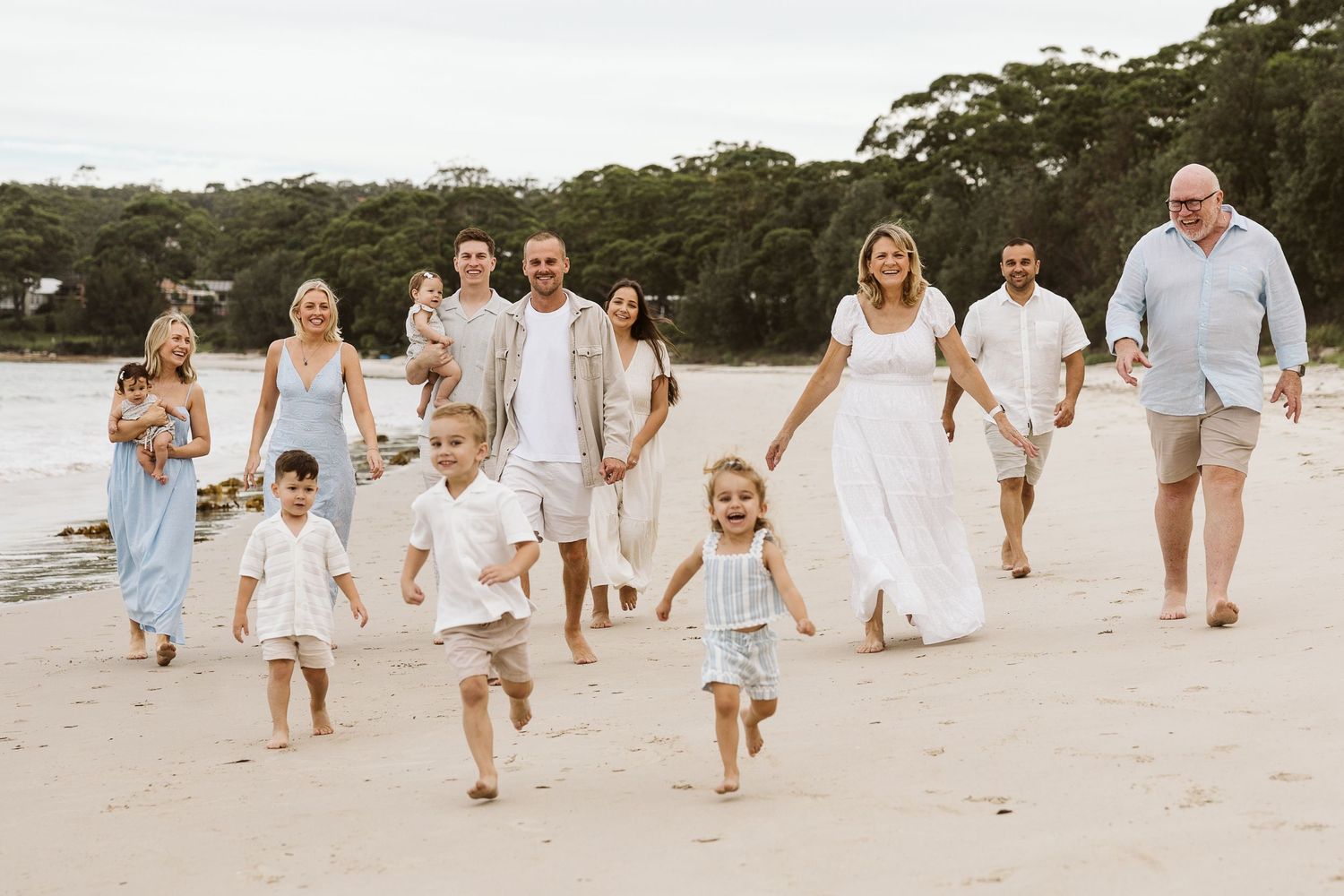 Large family group walking and running together on a sunny beach in coordinated outfits.