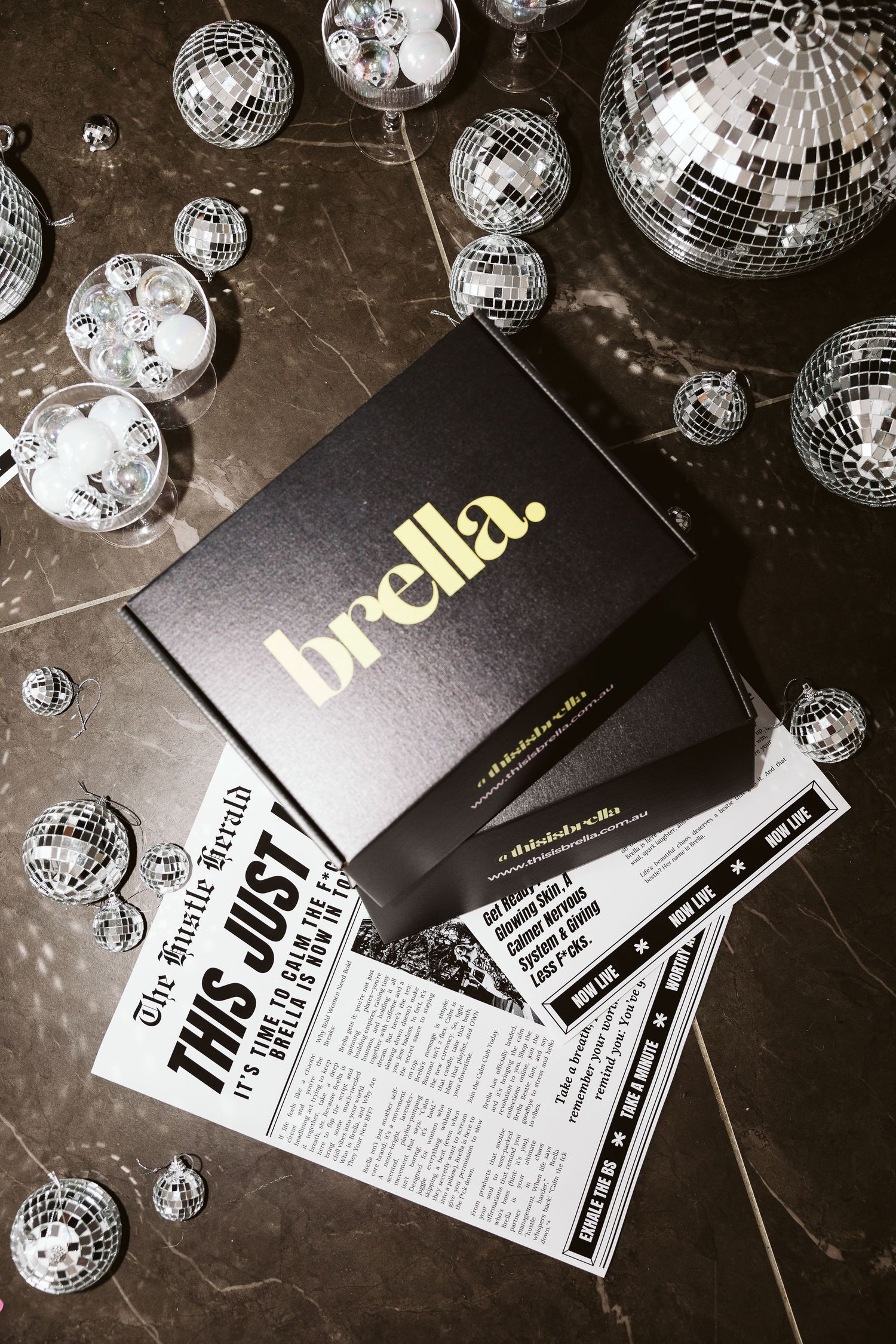 Brella black gift box with gold logo resting on branded newspaper surrounded by disco balls.