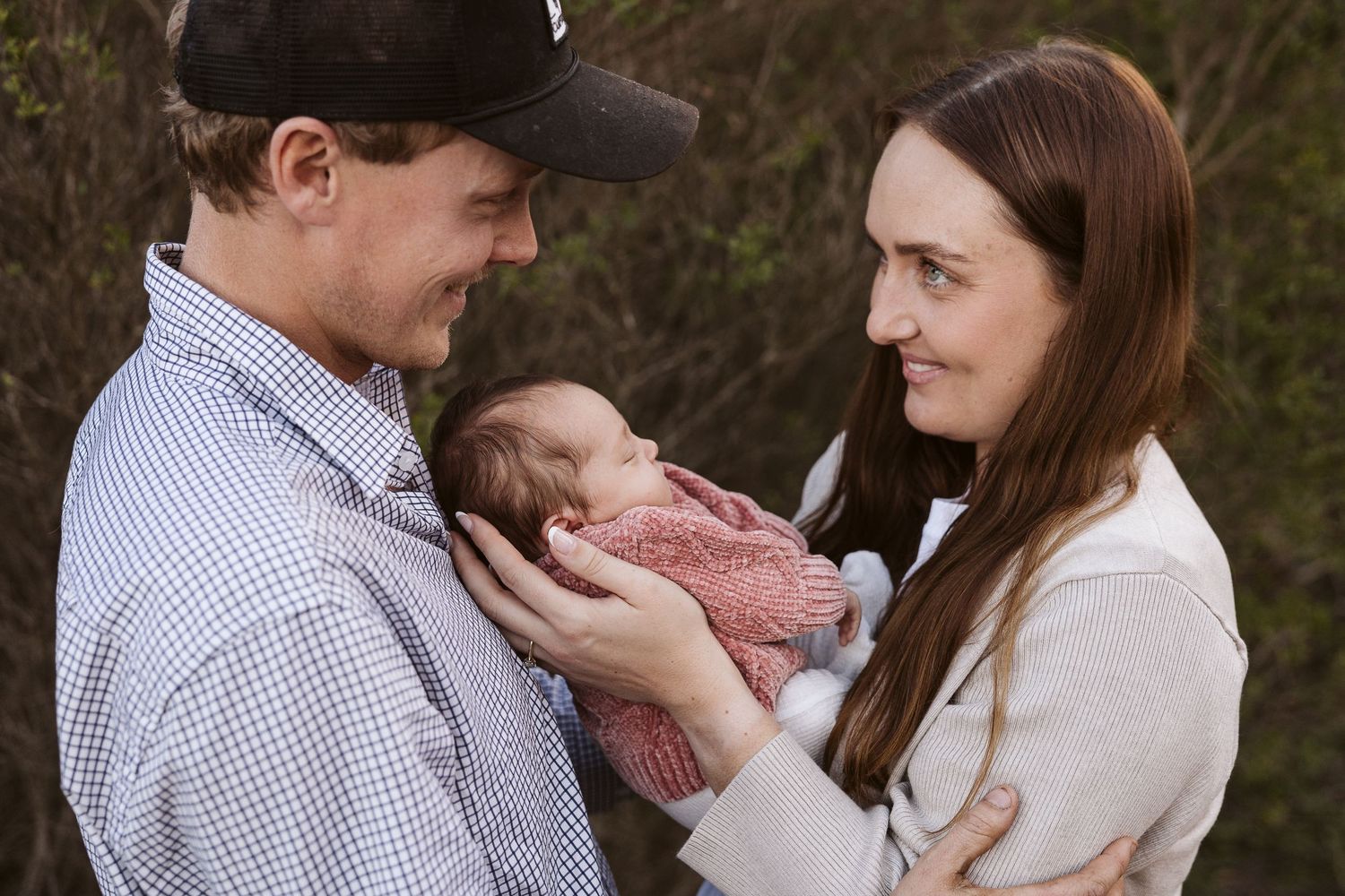 Young couple sharing a tender moment gazing at their newborn baby outdoors.