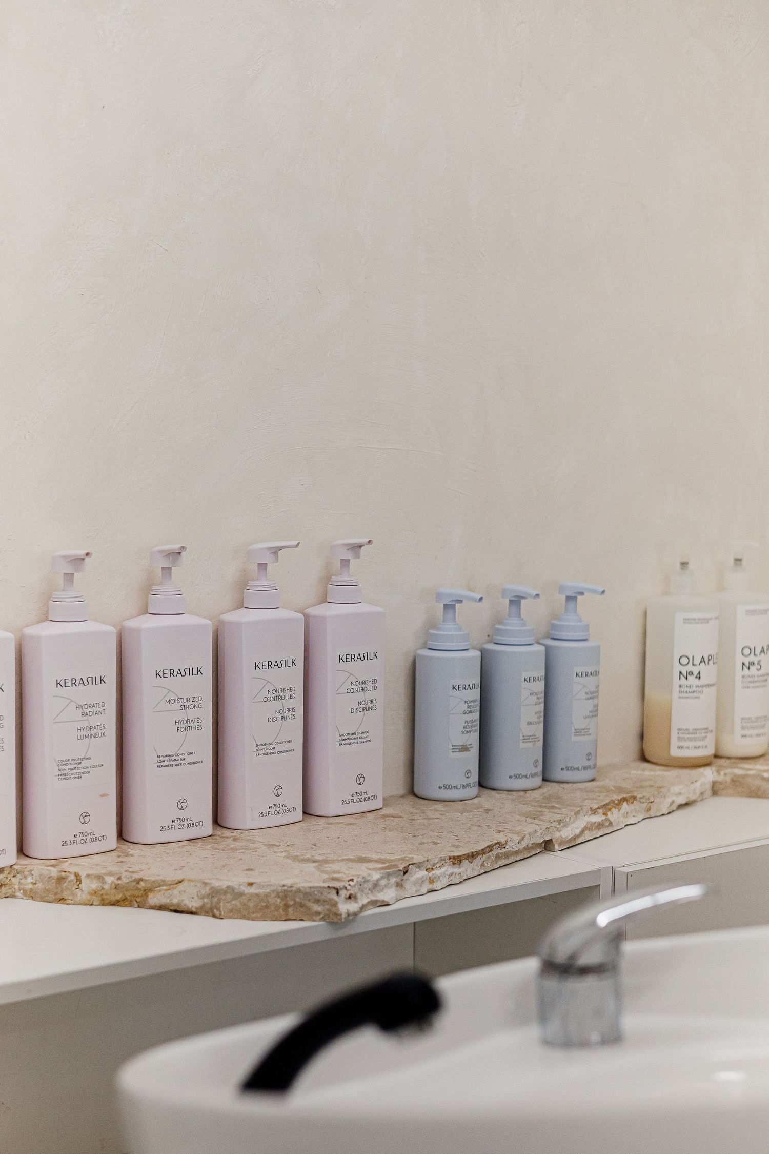 Kerasilk and Olaplex hair care products lined up on a marble shelf above a salon basin.