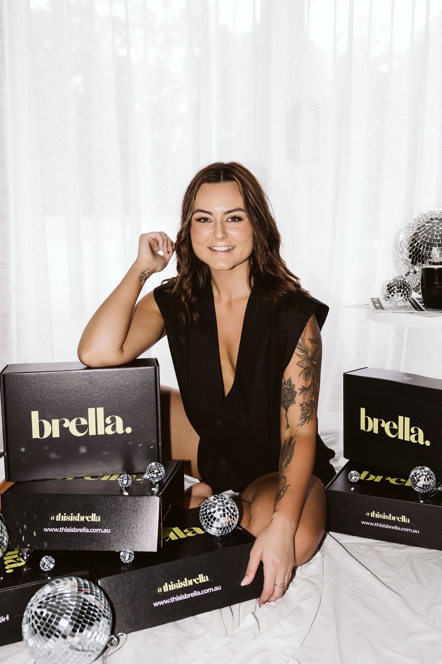 Smiling brunette woman in black outfit posing with Brella branded boxes and disco balls.