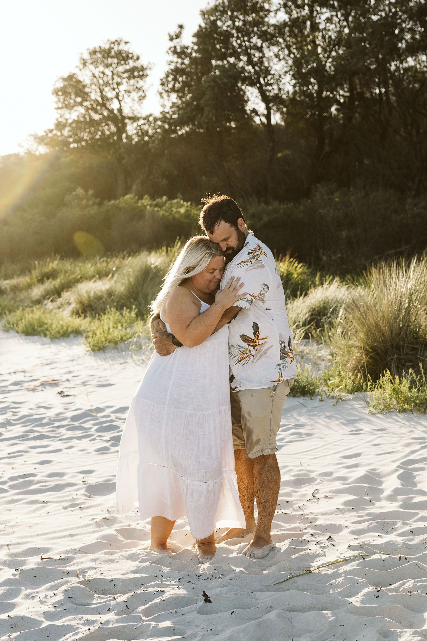 Couple embracing romantically on white sand beach at golden sunset.