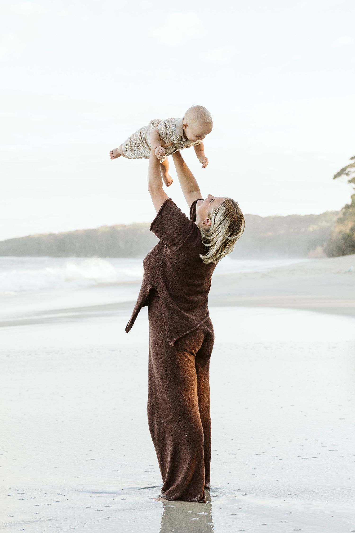 Motherhood photoshoot with baby on a peaceful sandy beach at sunset.
