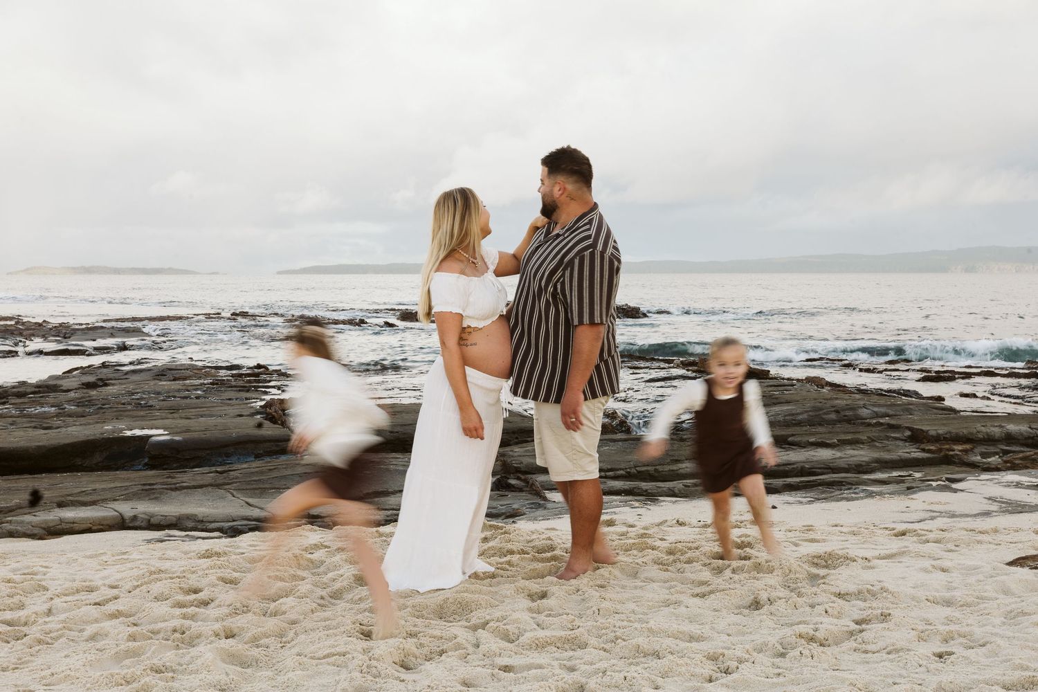 Couple standing on beach while two young children run around them playfully.