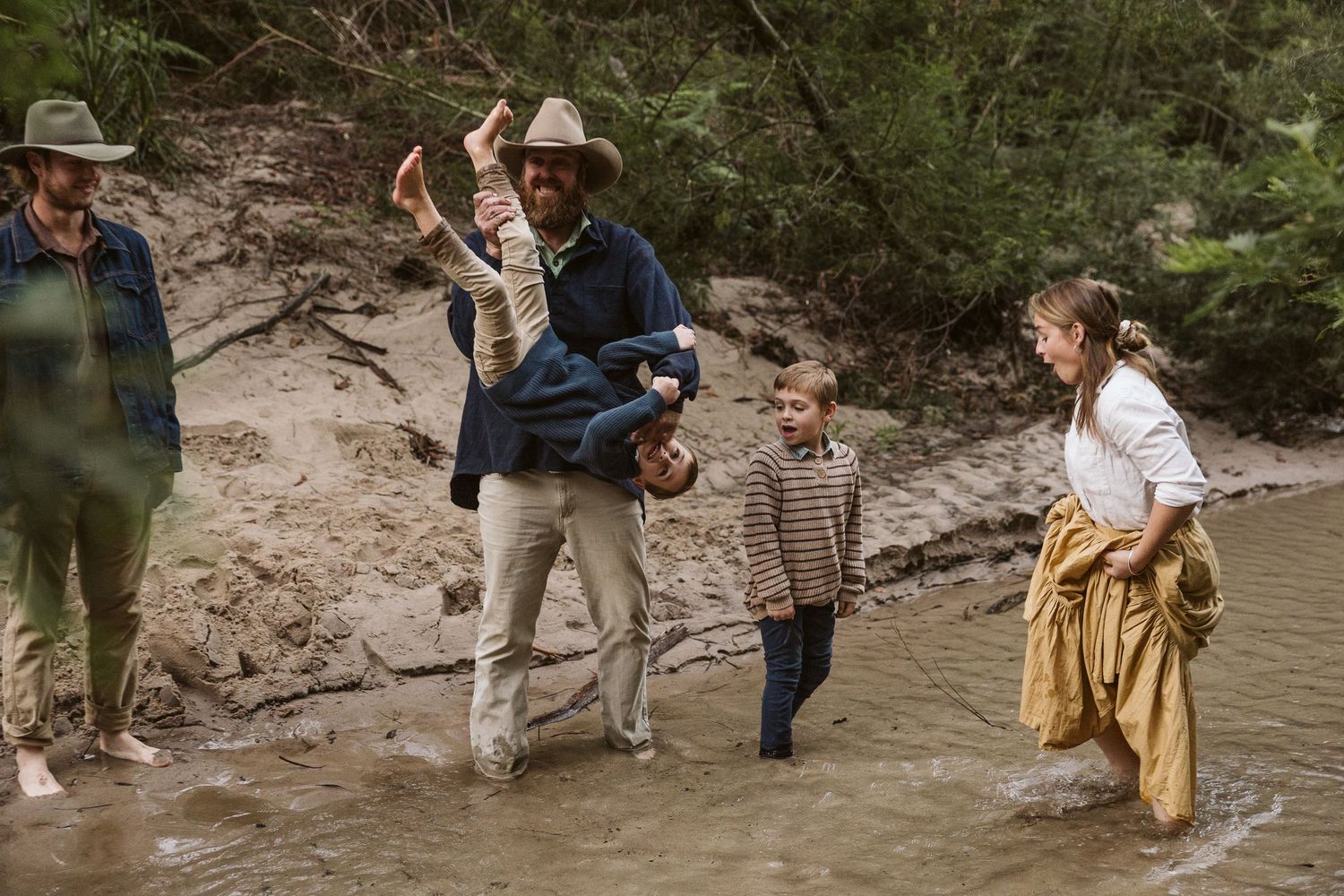 Family wading through a shallow creek in a natural bush setting with children and adults splashing.