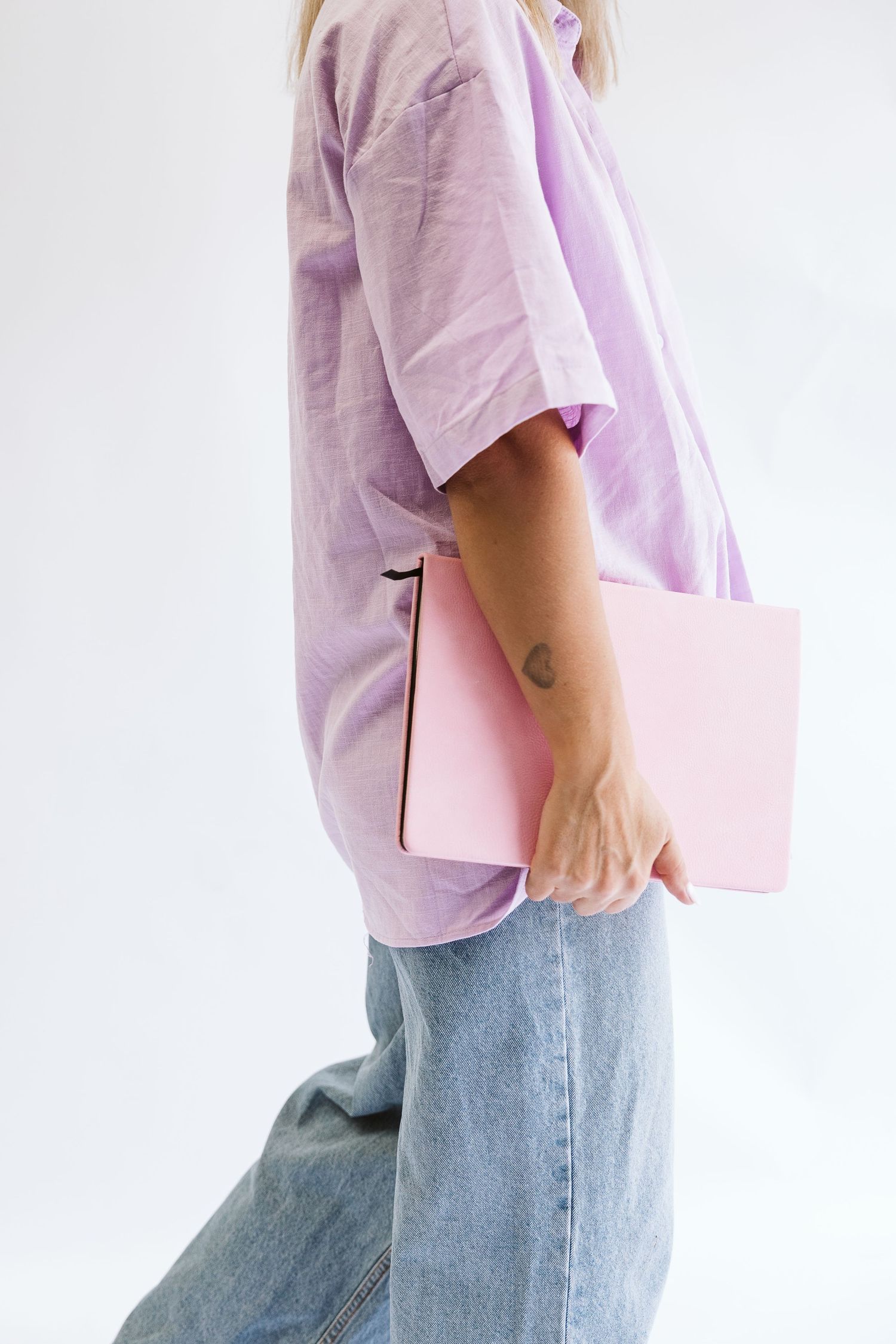 Woman in lilac linen shirt and jeans holding pink notebook against white background.