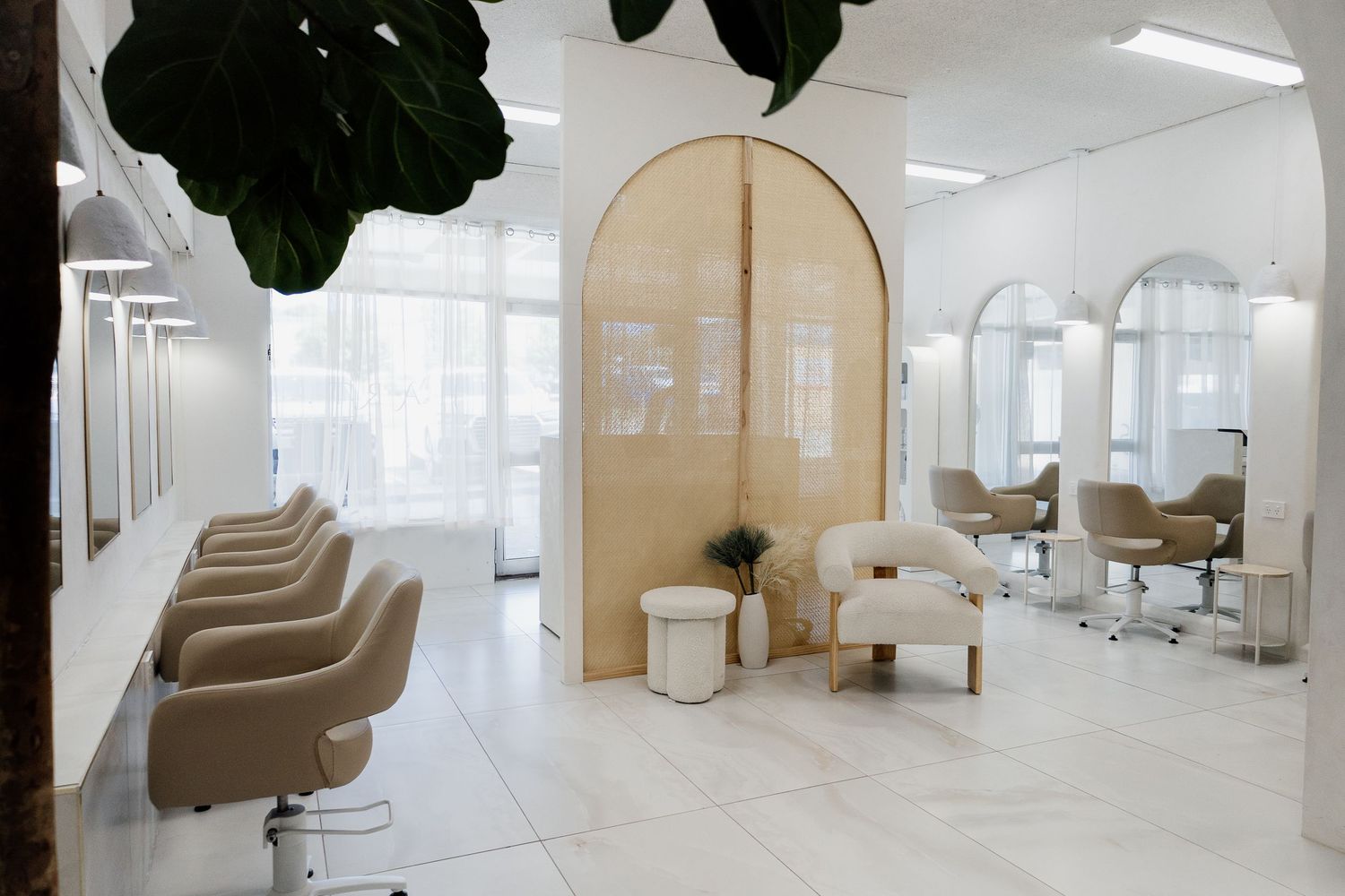 Elegant modern hair salon with beige styling chairs, arched mirrors, and marble floors.