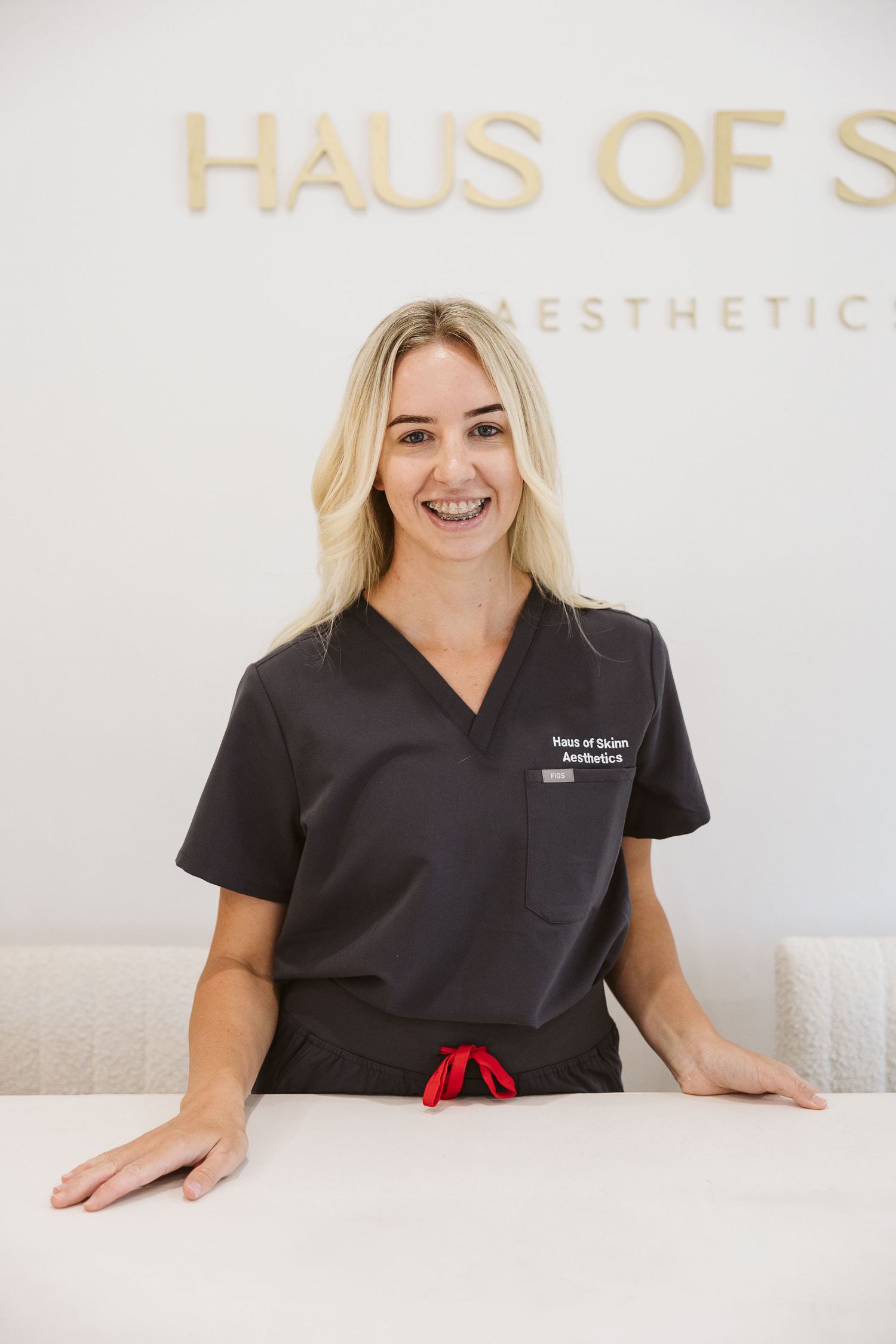 Smiling blonde woman in black scrubs at Haus of Skinn Aesthetics reception desk.