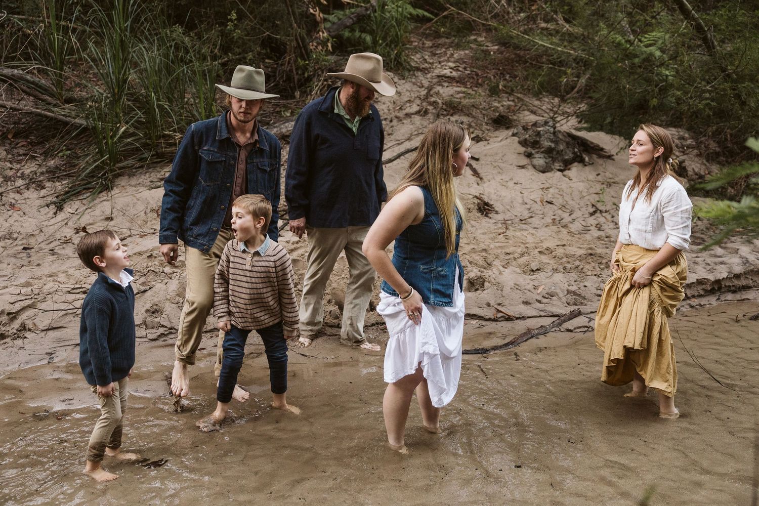 Family wading in a shallow creek surrounded by lush greenery on a casual outdoor adventure.