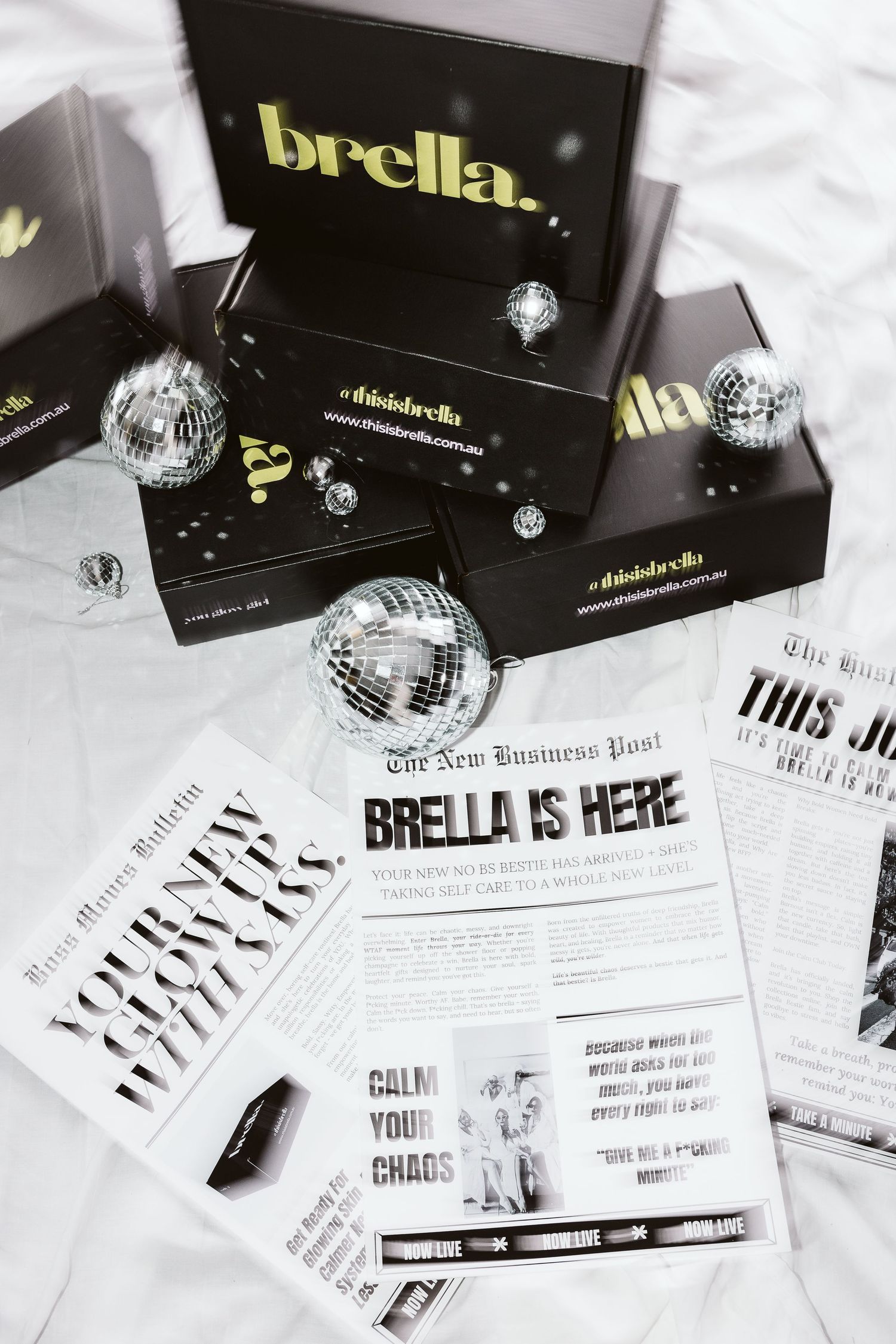Brella branded black boxes and newspapers with silver disco balls on white background.