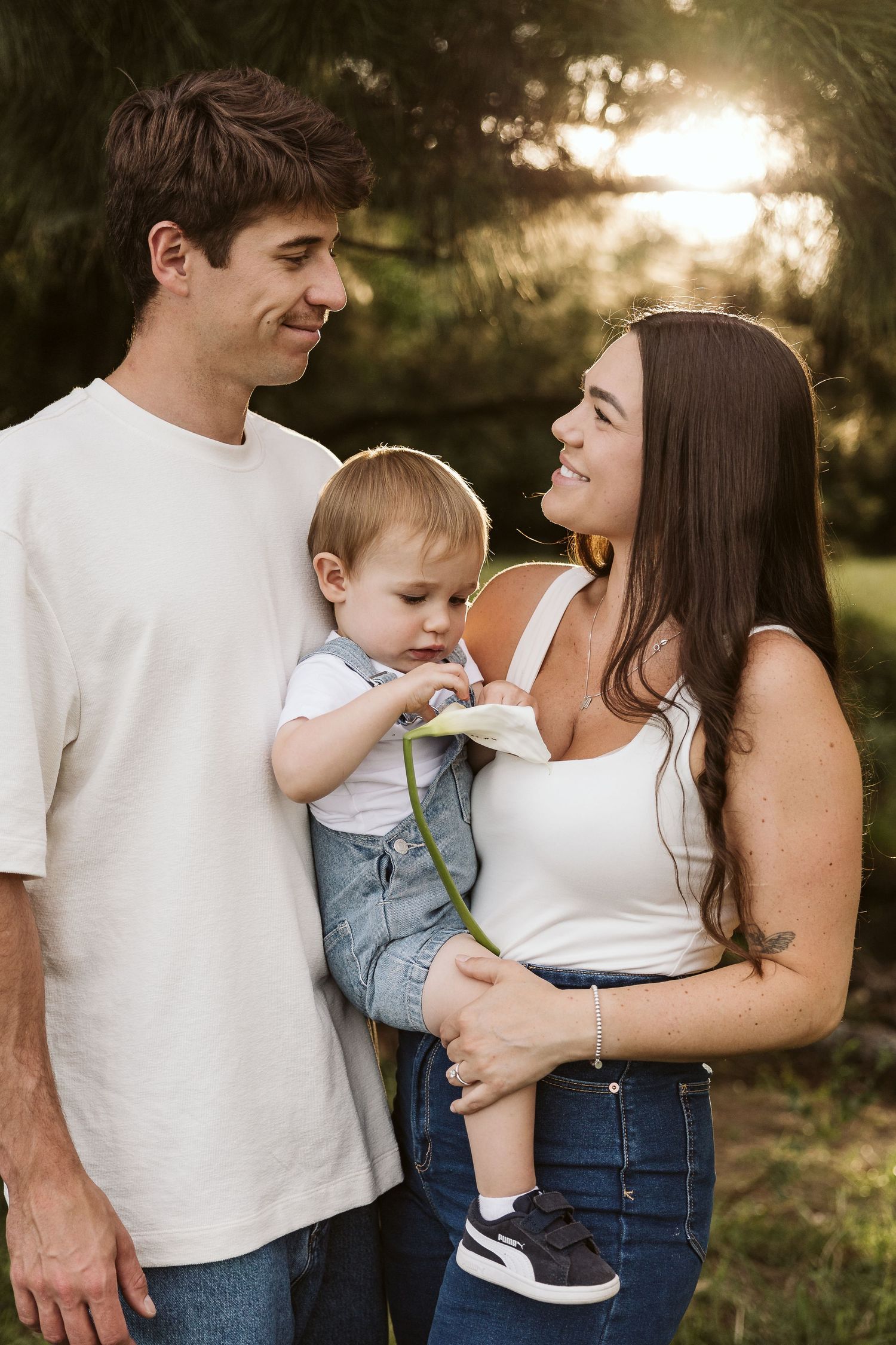 Happy young family with baby boy holding a flower together outdoors at golden hour.