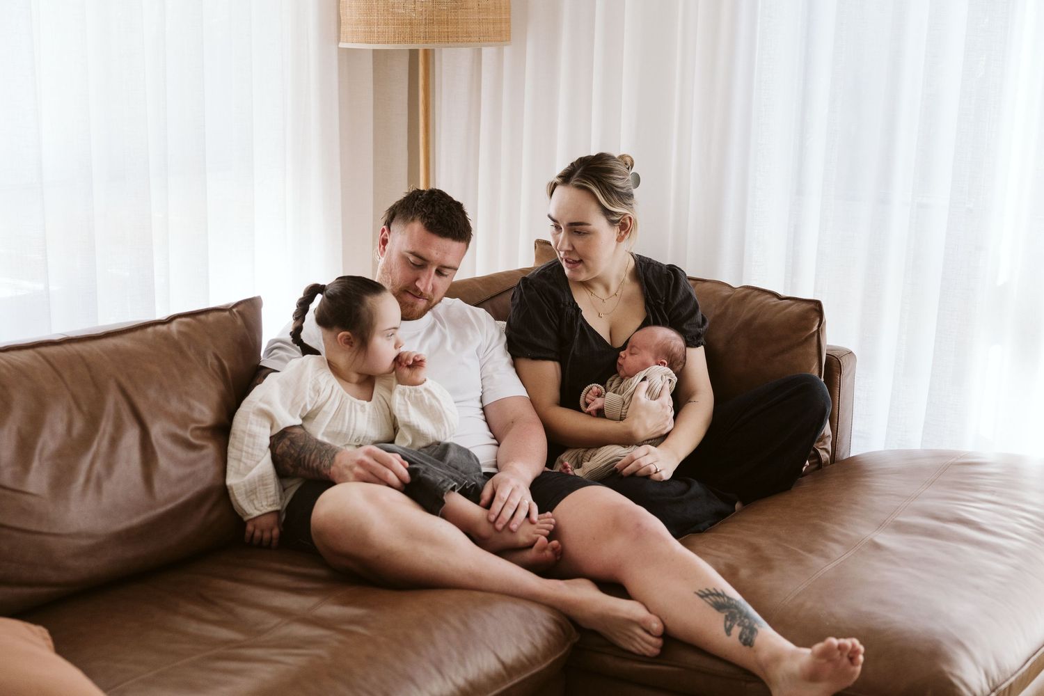 Family with two children sitting together on brown leather couch at home. Newborn photoshoot