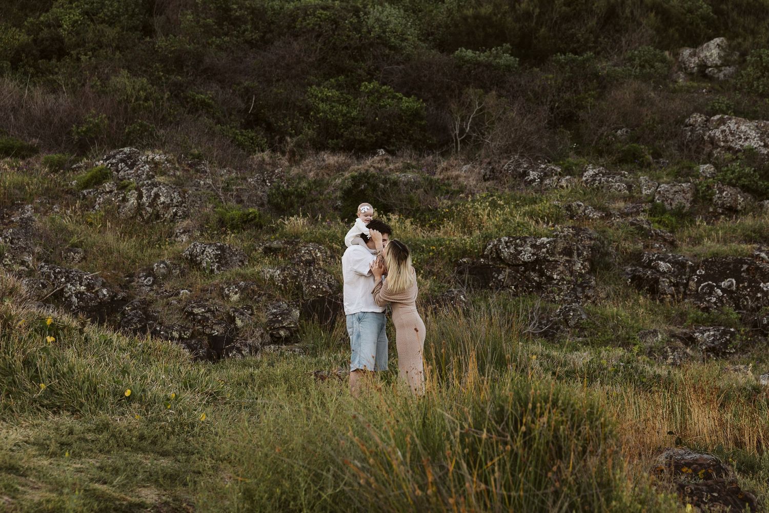 Couple embracing in a lush green meadow with rocky hillside backdrop during an outdoor engagement session.