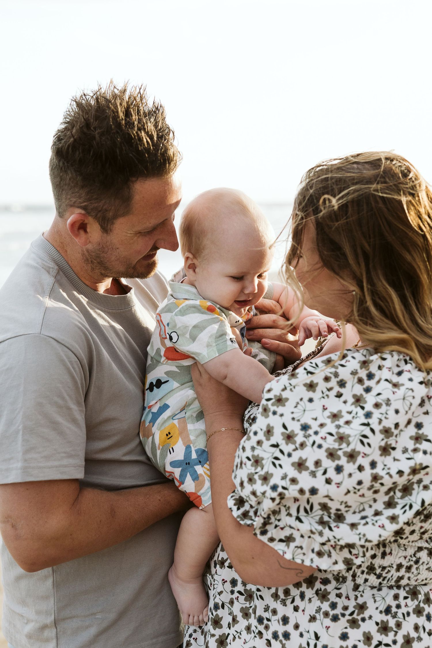Happy couple holding their smiling baby at the beach, sharing a tender family moment outdoors.