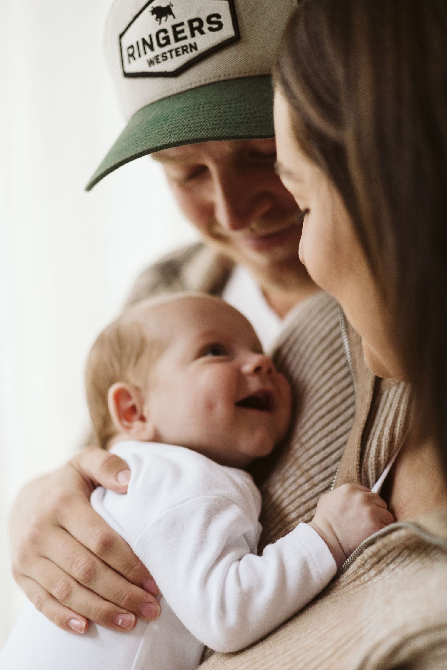 Smiling parents in casual wear lovingly hold their laughing newborn baby.