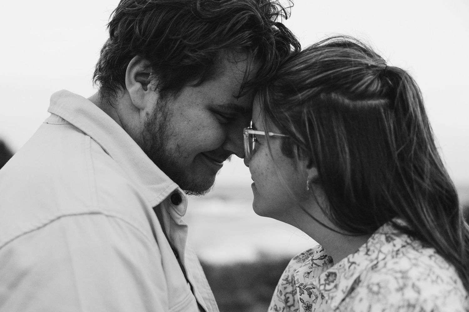 Black and white close-up of couple touching foreheads and smiling tenderly in an outdoor setting.