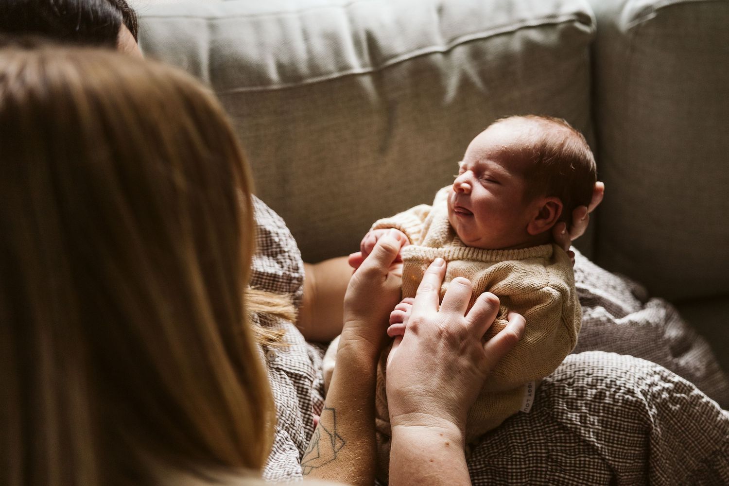 Mother tenderly holding and looking down at alert newborn baby wrapped in cozy knit blanket.