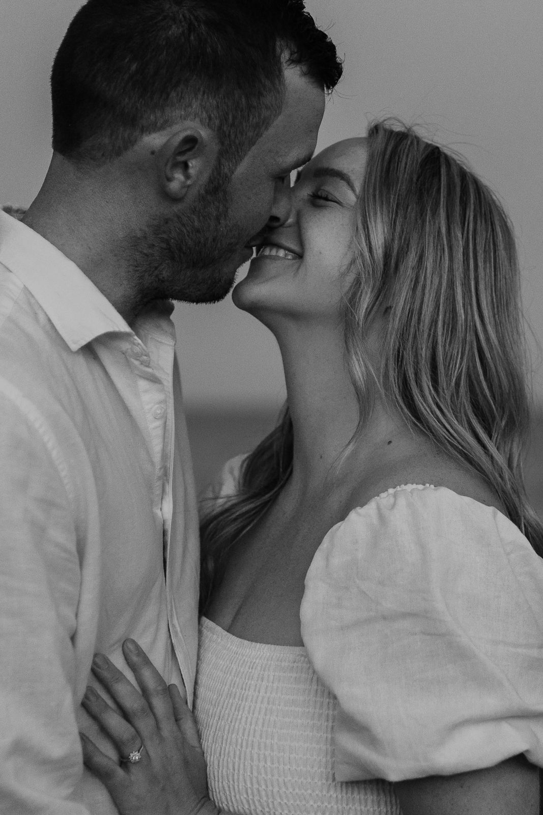 Black and white intimate portrait of a smiling couple about to kiss during a romantic engagement shoot.